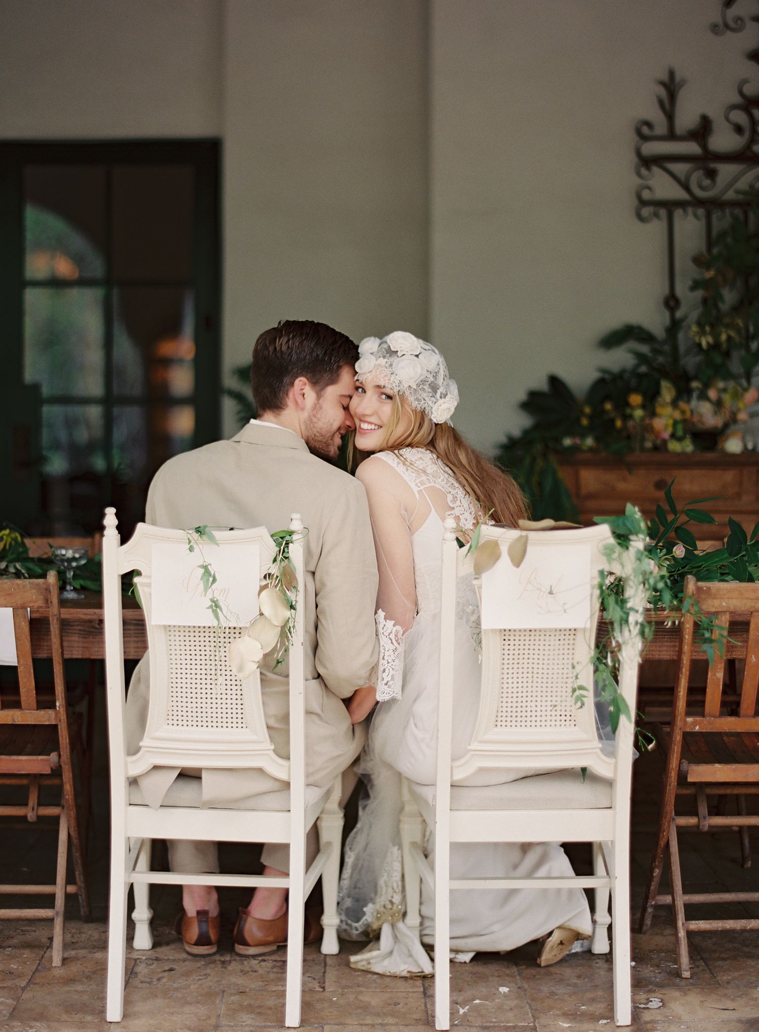 Romantic white wooden chairs decorated with greenery on an outdoor patio.