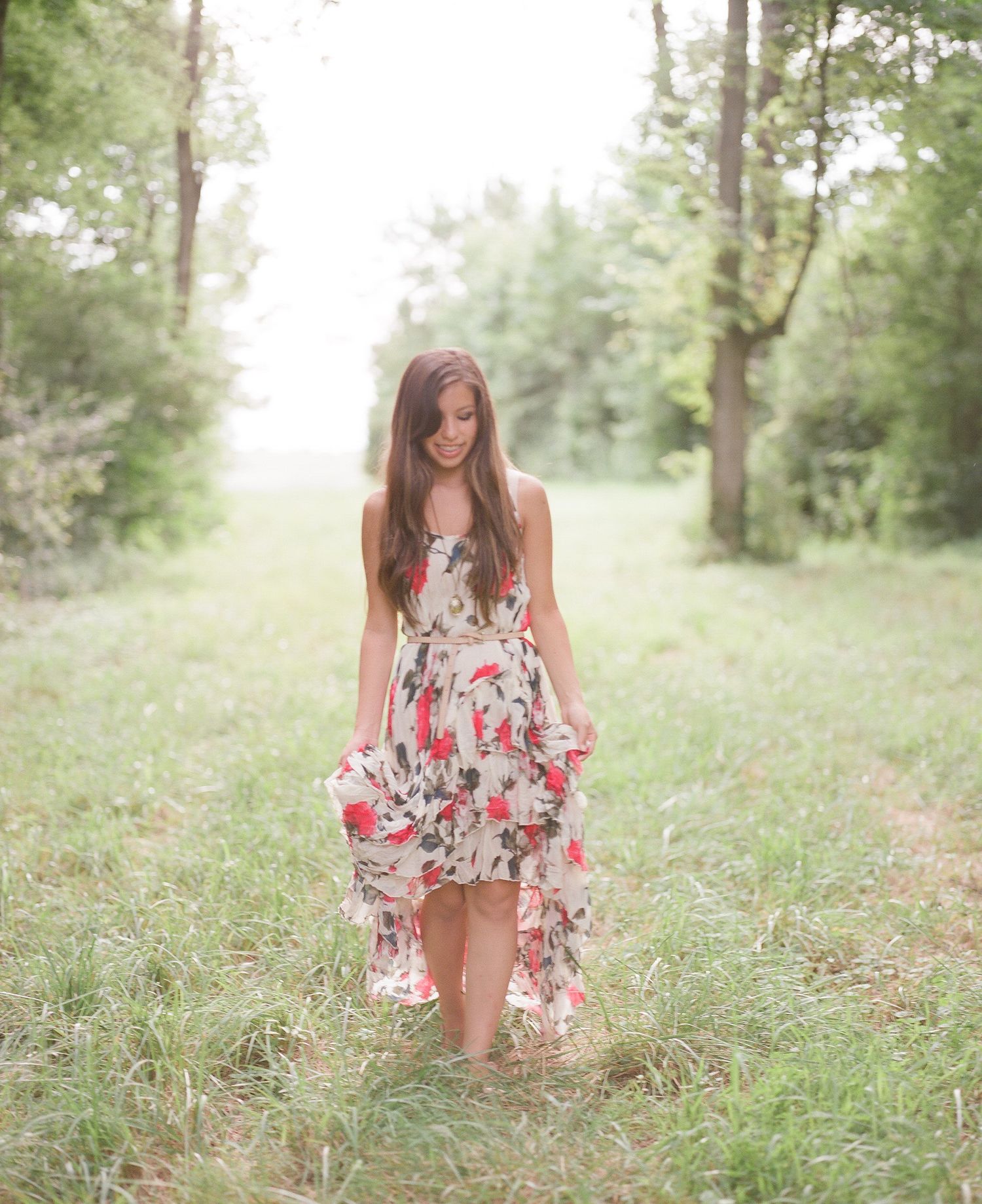 A floral summer dress flows in the breeze as someone poses in a grassy meadow with trees.