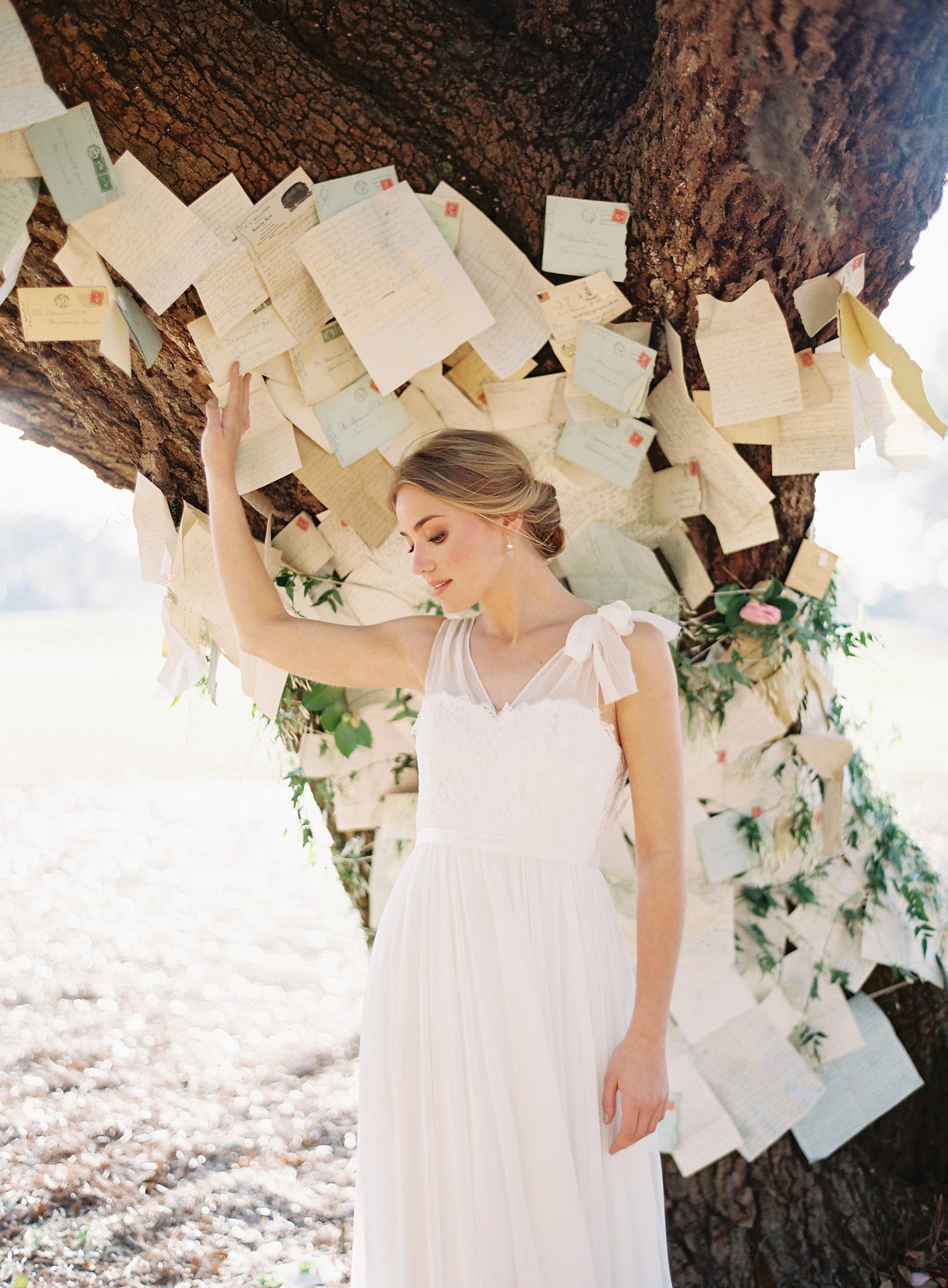 Wedding dress detail shot under a tree decorated with hanging paper and greenery.