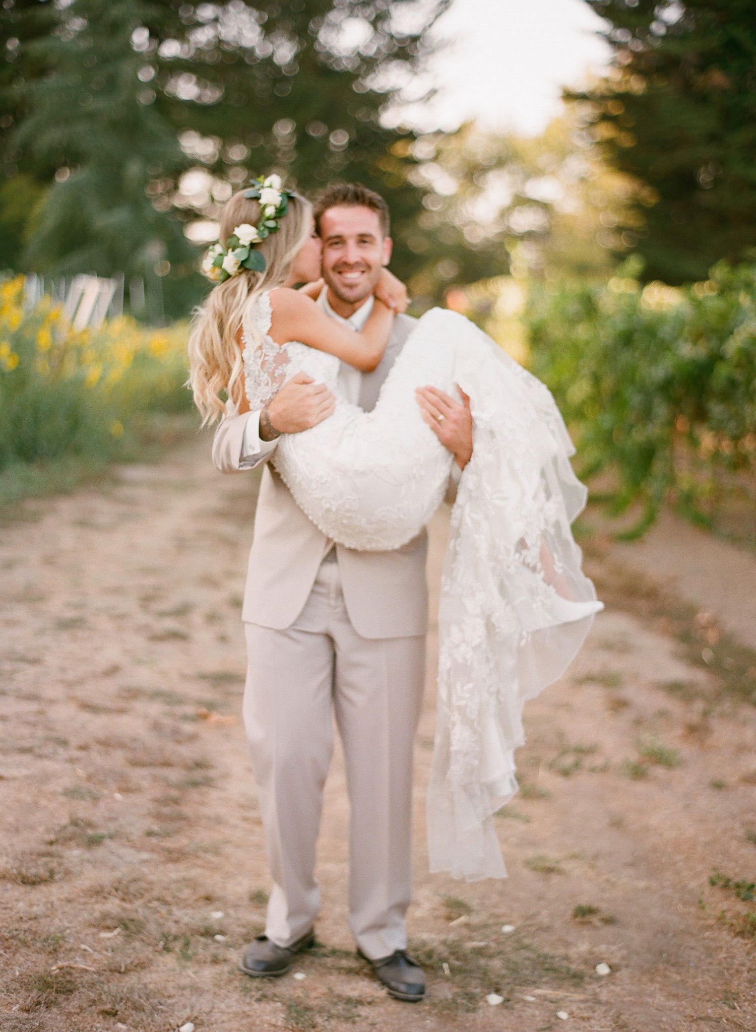 Wedding couple in white attire playfully dancing in an outdoor garden setting.