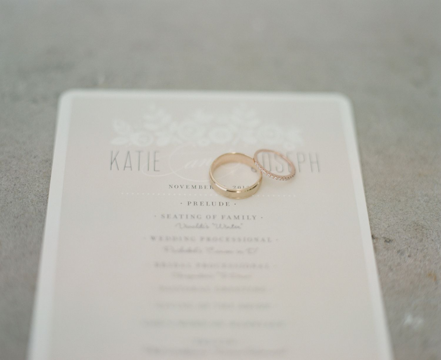 Wedding invitation cards with rose gold rings placed on a light gray surface.