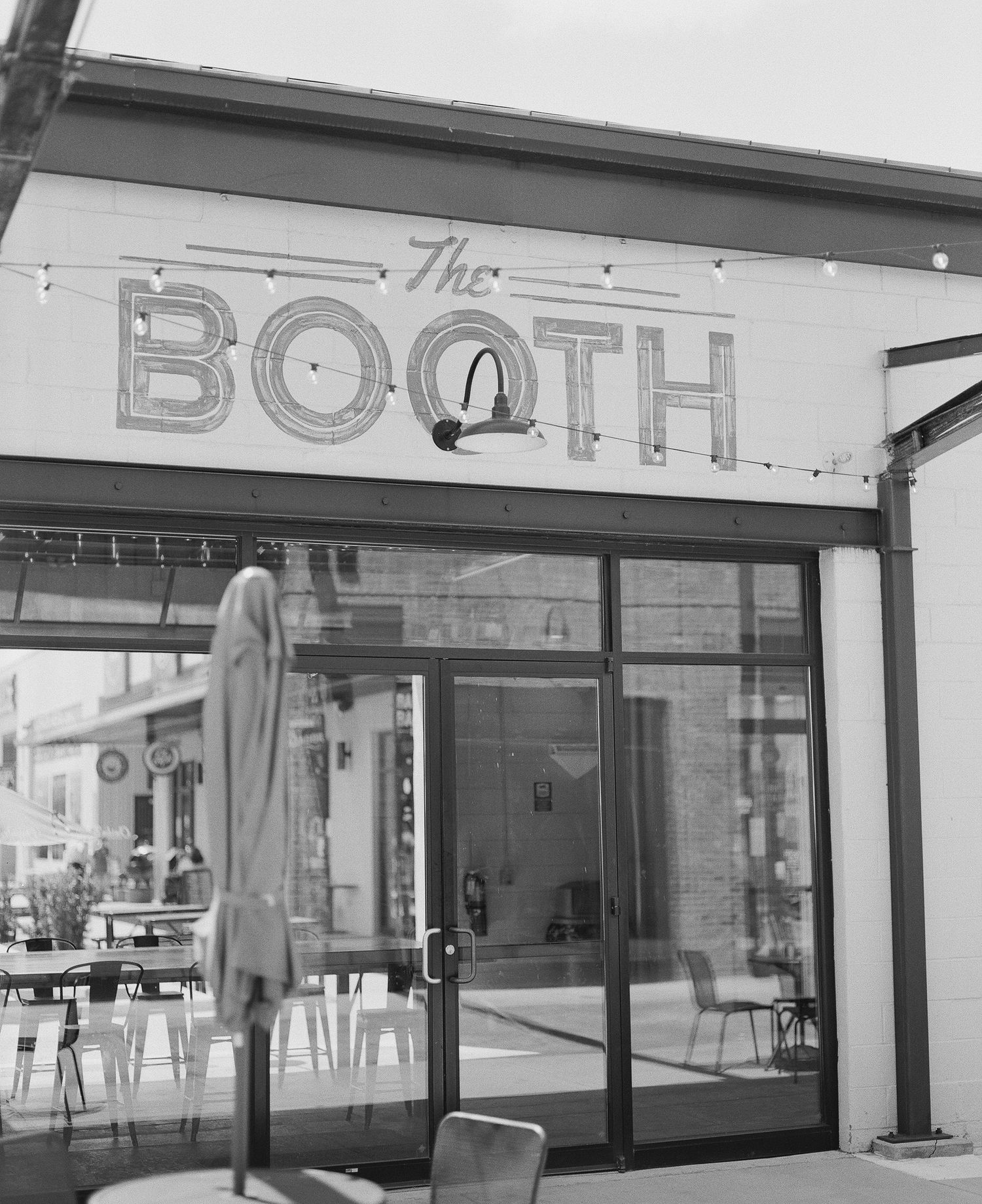 Black and white photo of The Booth restaurant exterior with large glass storefront and outdoor seating area.