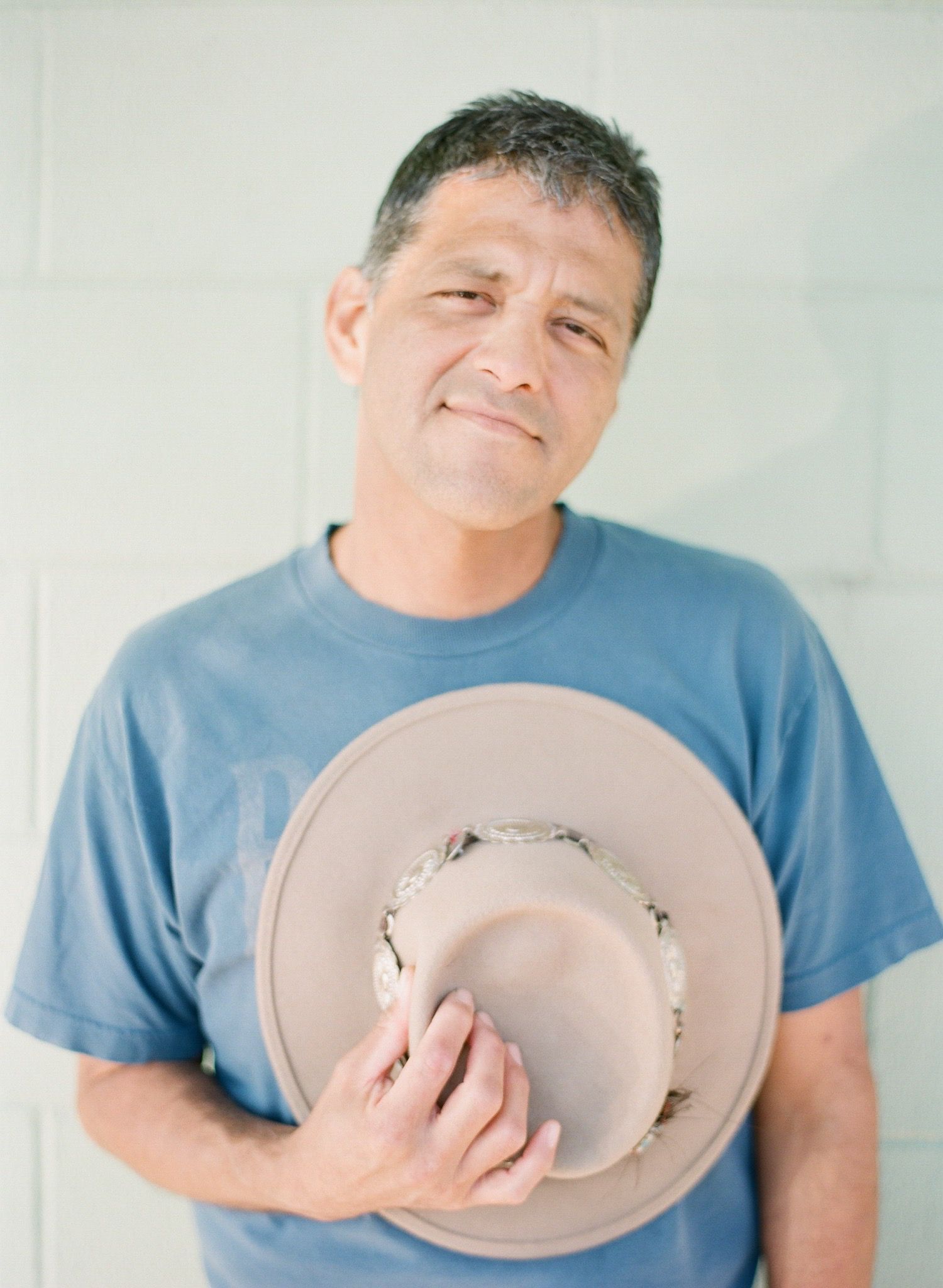 Person in blue t-shirt holding and examining a light colored cowboy hat in a series of photos.