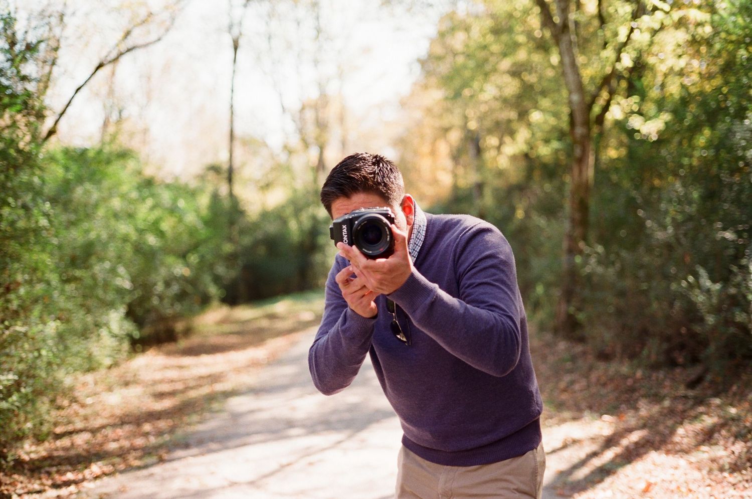 Photographer in navy sweater taking pictures on a wooded trail.