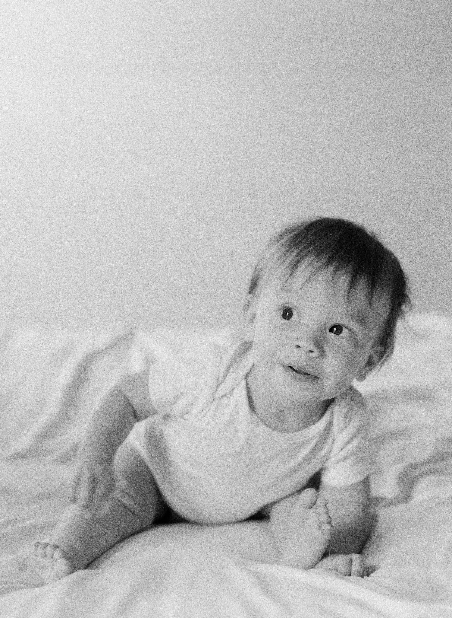 Black and white photo series of baby lying on white bedding.