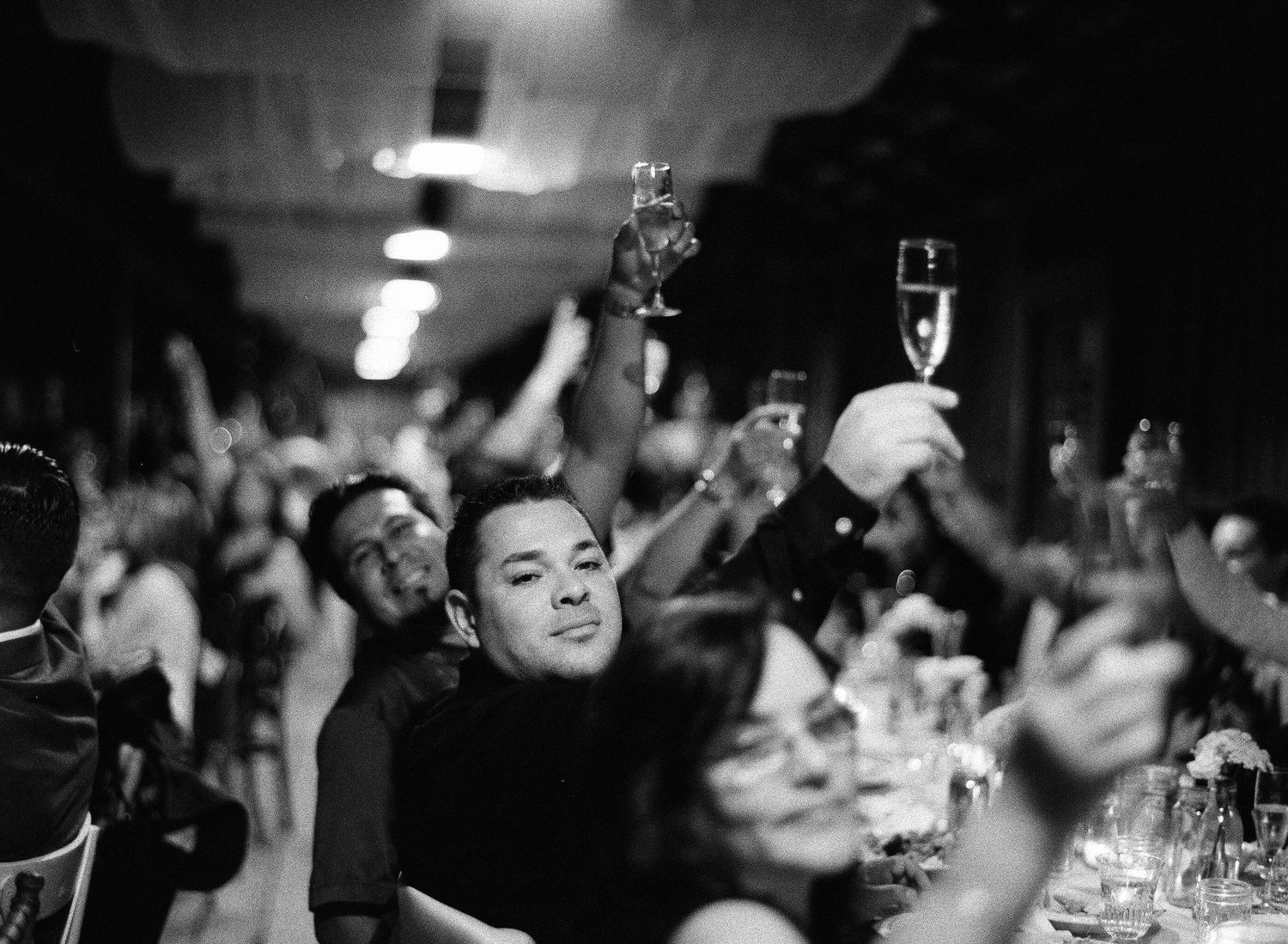 Dark reception hall filled with celebrating guests raising their glasses in celebration.