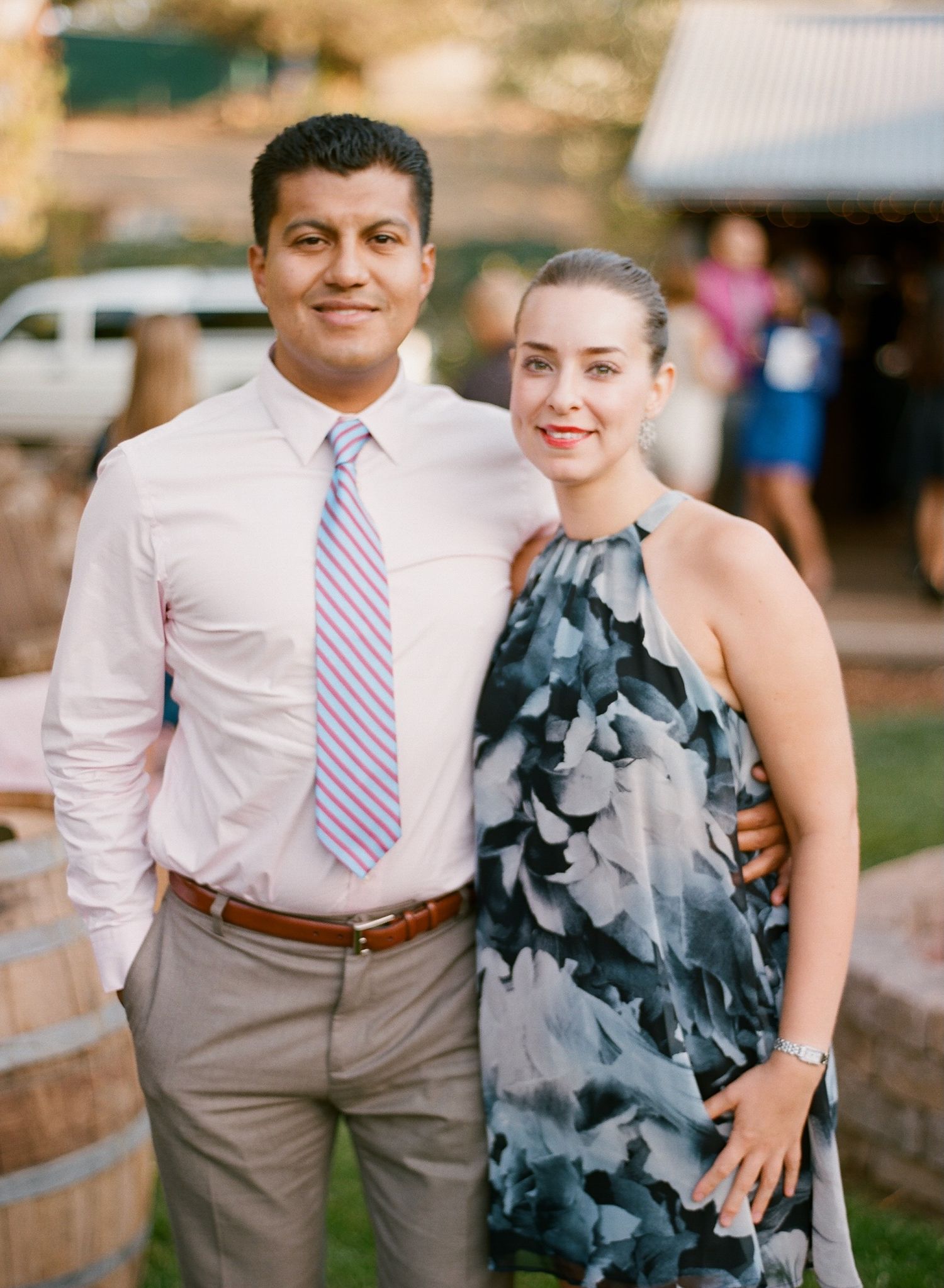 Couple in formal attire posing together outdoors, with the woman wearing a blue-gray dress.