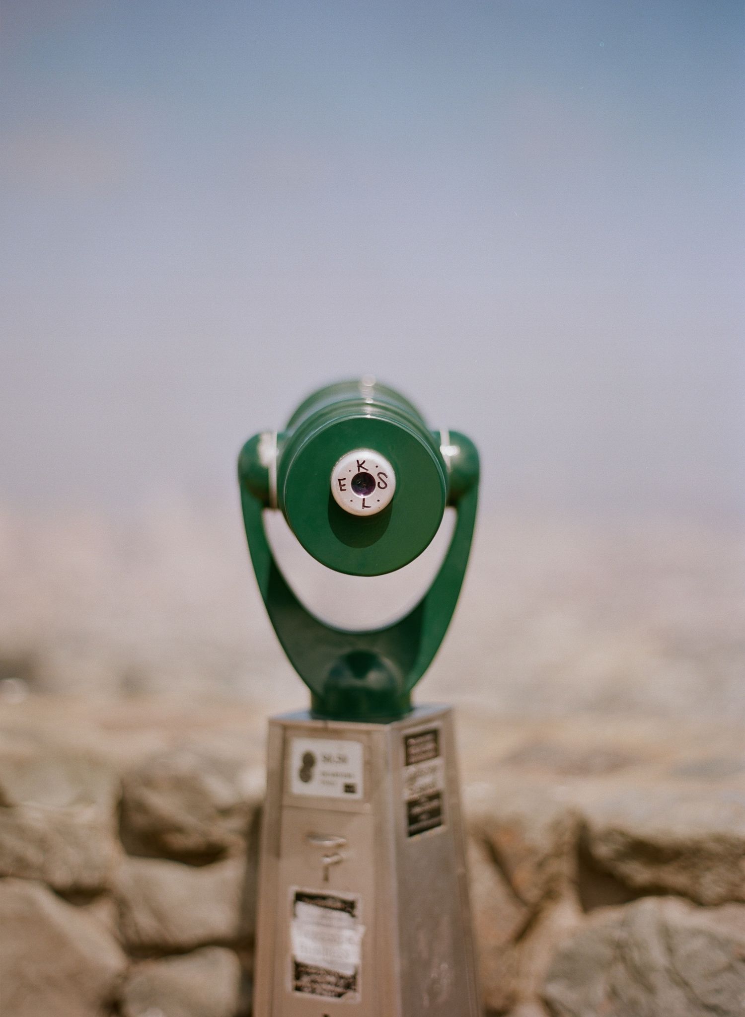 Green viewfinder scope mounted on metal stand against blurred desert background.