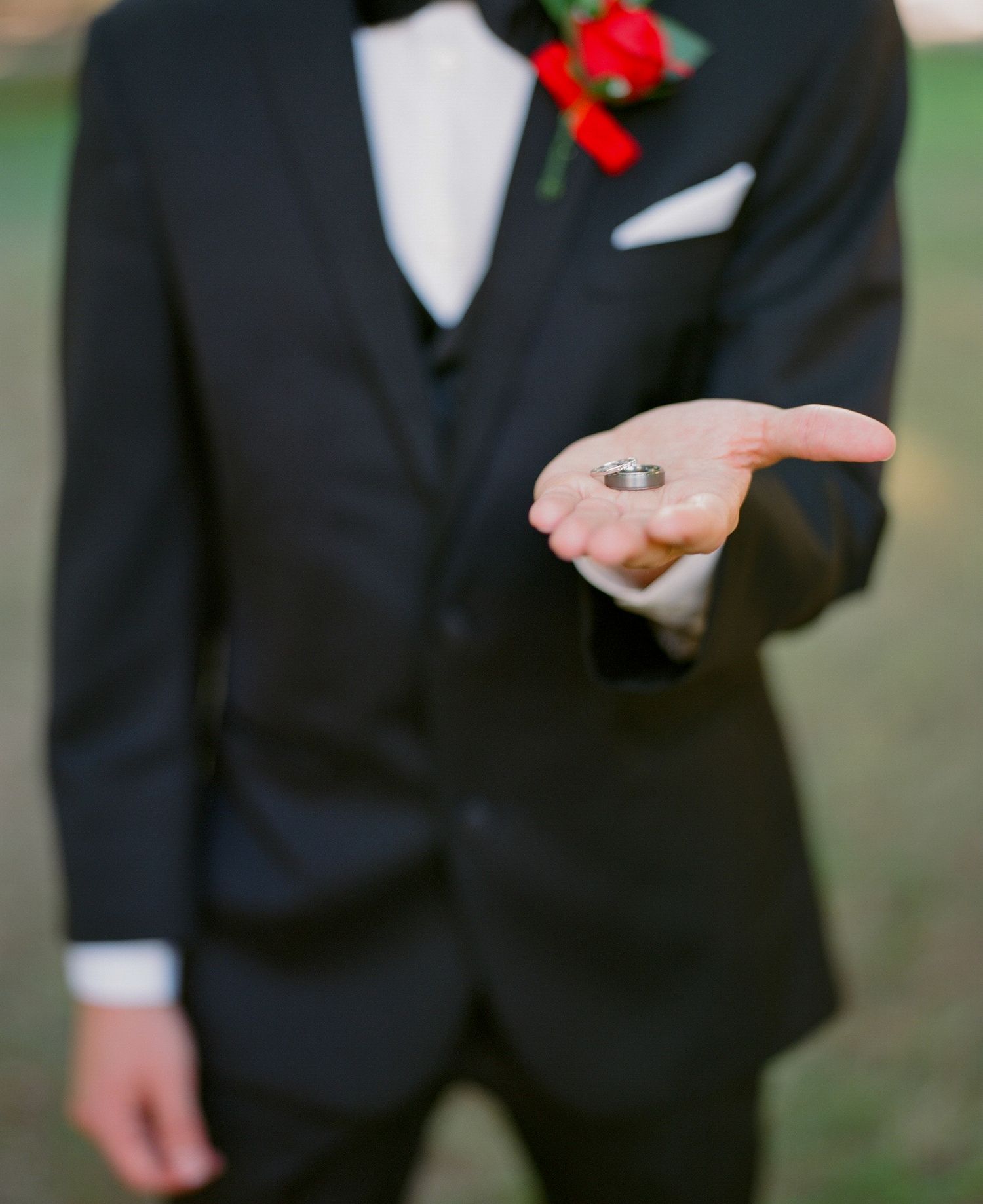 Detail shot of black tuxedo with red boutonniere against green background.