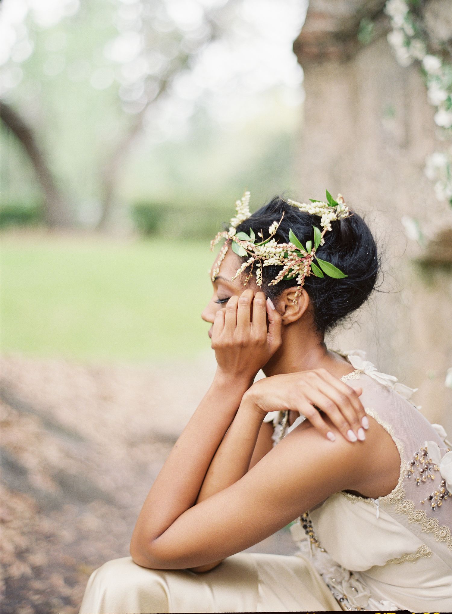 Bride wearing floral crown and lace dress poses artistically on natural ground.