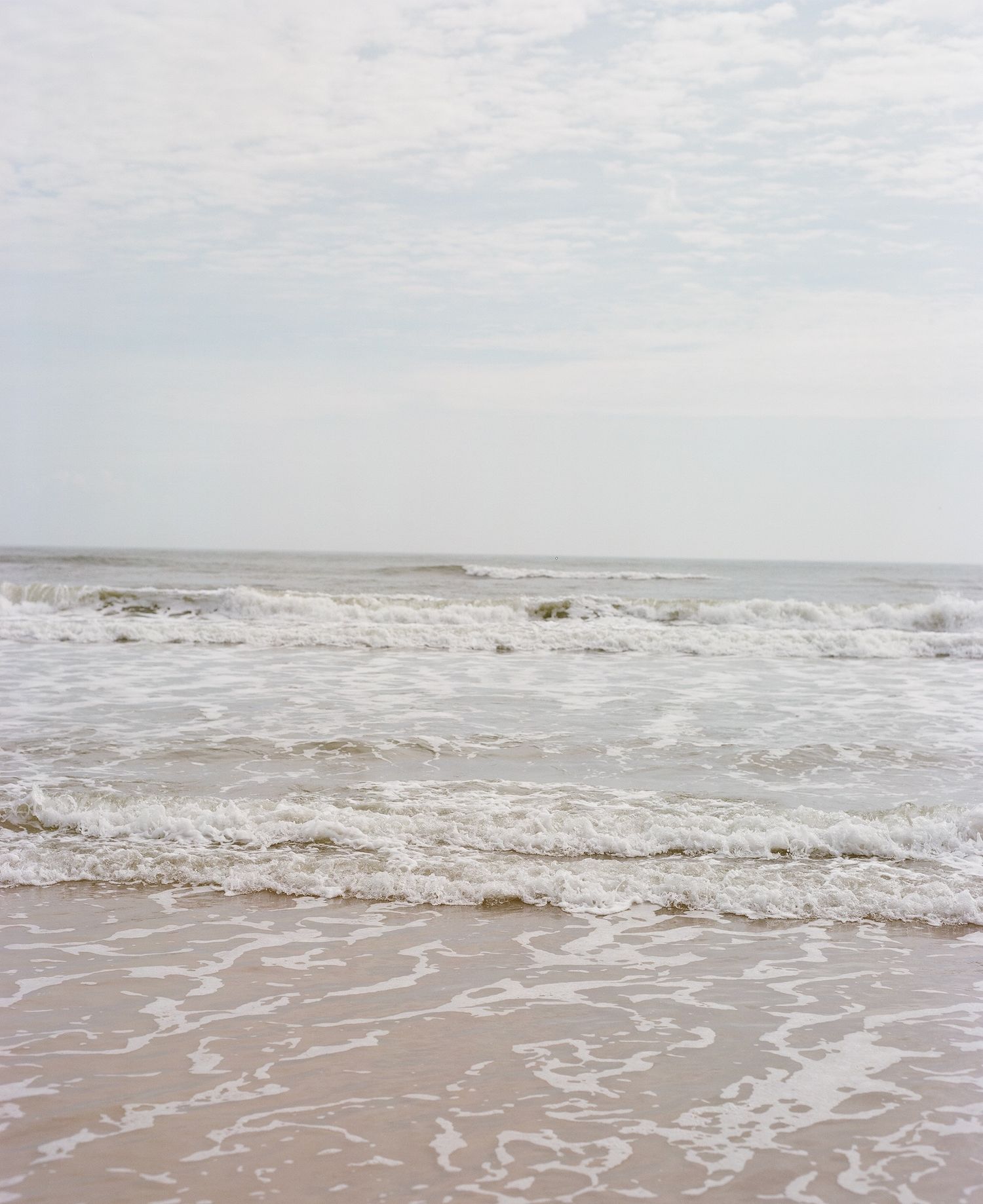 Panoramic sequence of ocean waves rolling onto a sandy beach under an overcast sky.