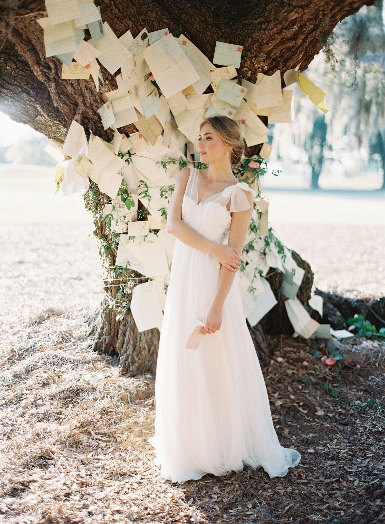 A white dress flows gracefully under a tree decorated with hanging paper and ivy.