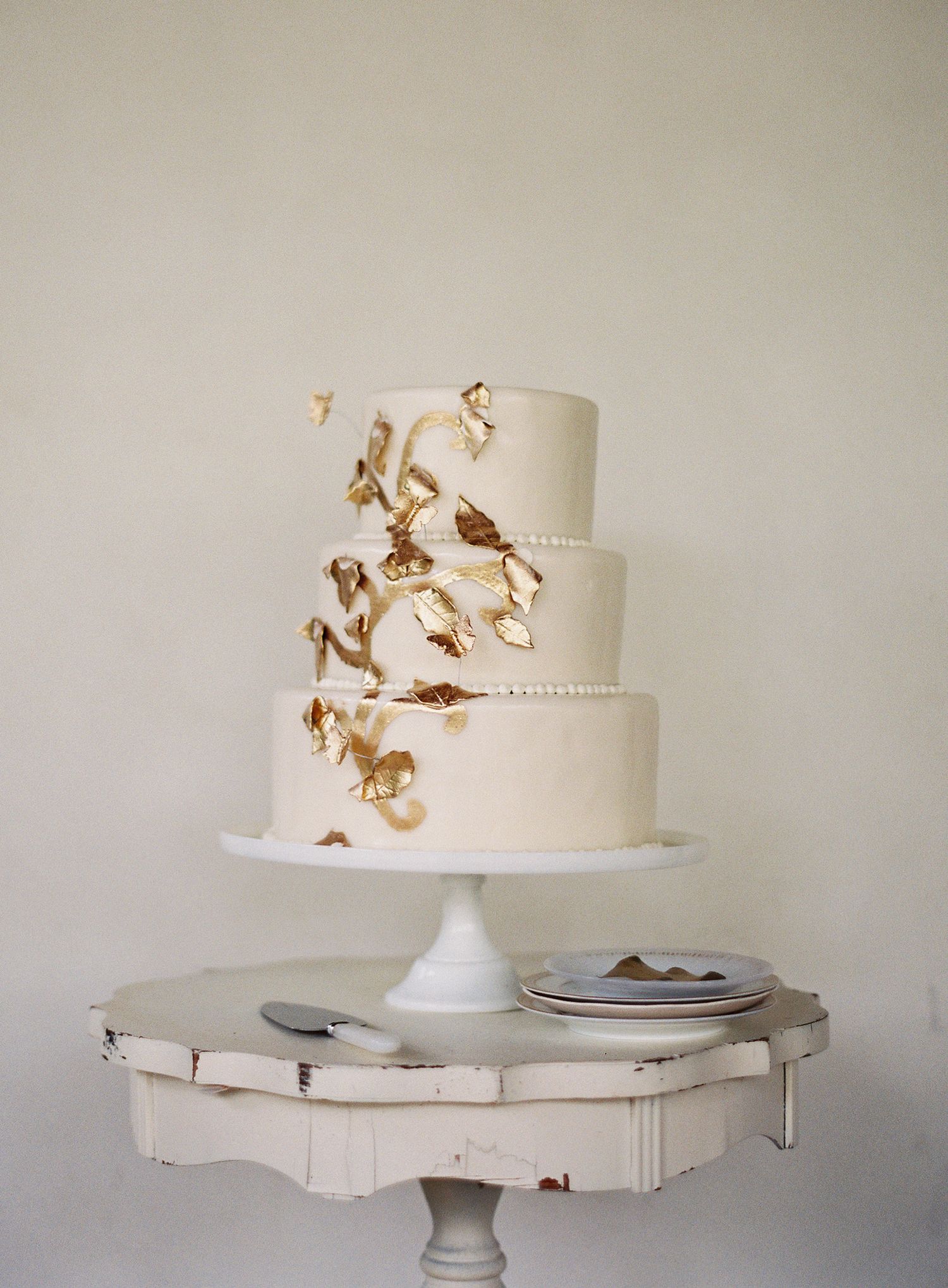 Minimalist white wedding cake with gold metallic accents displayed on vintage white pedestal.
