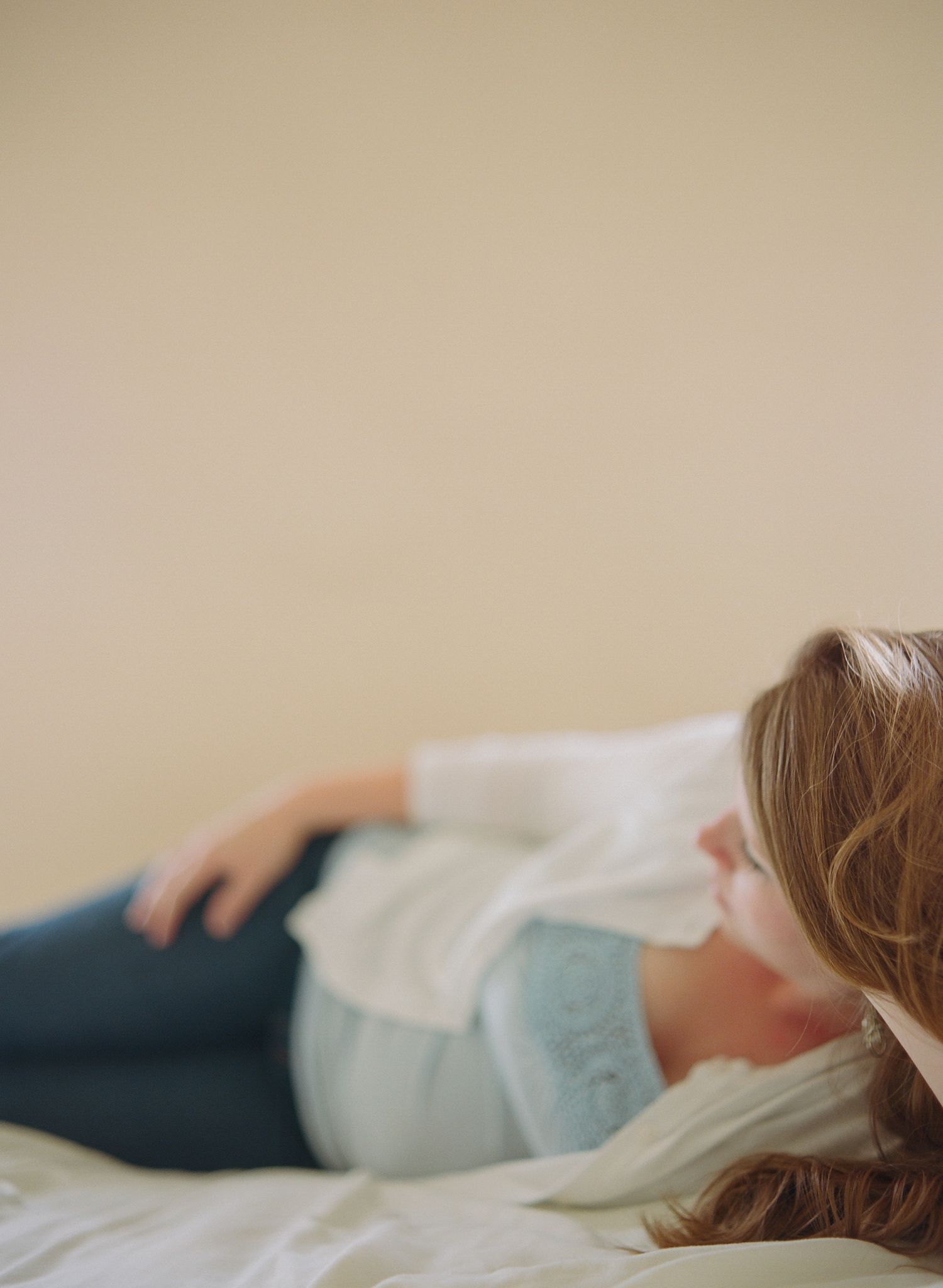 Serene side view of someone resting on white bedding in soft natural light.