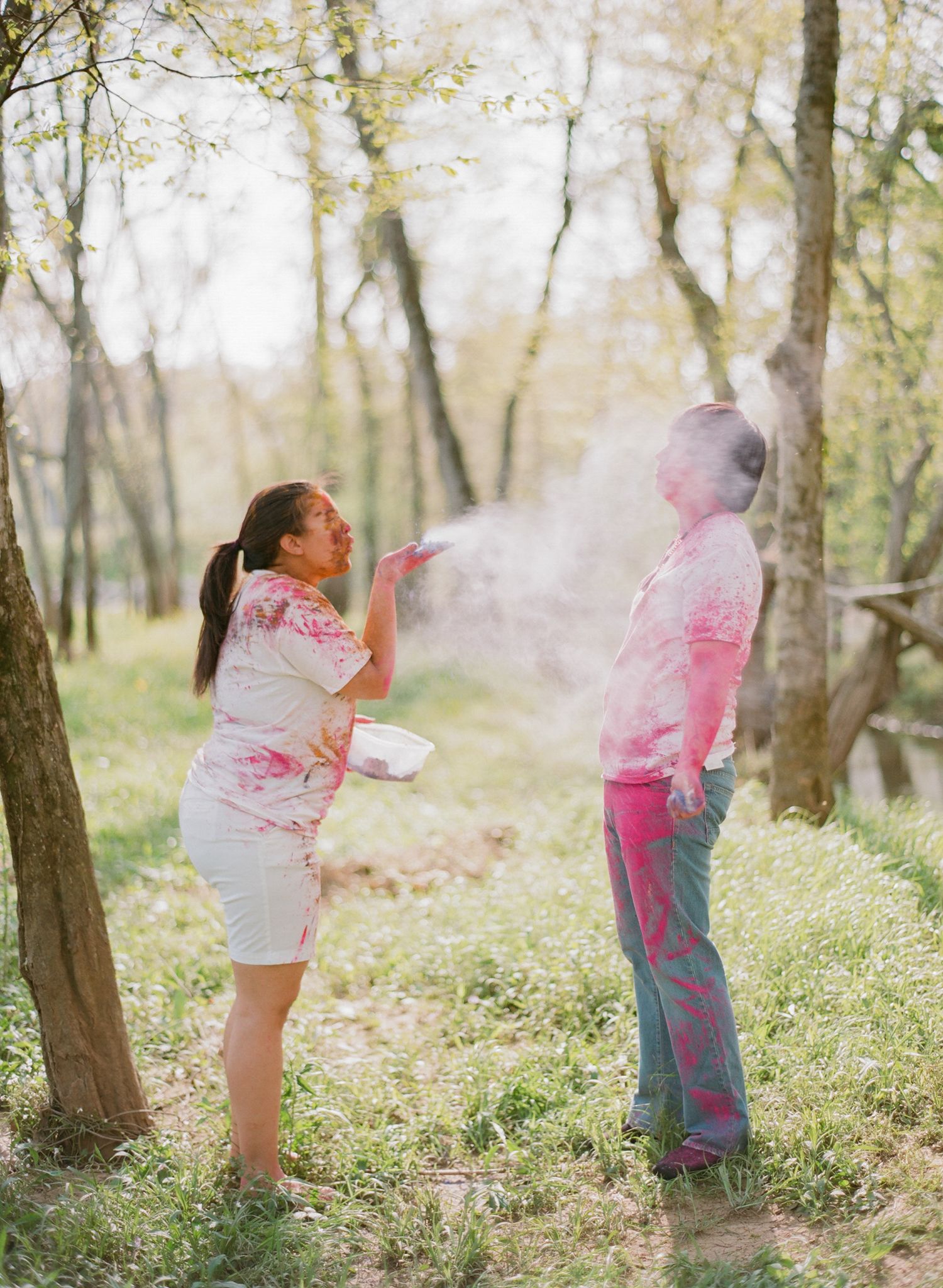 A playful sequence of pink powder being thrown in a wooded outdoor setting.