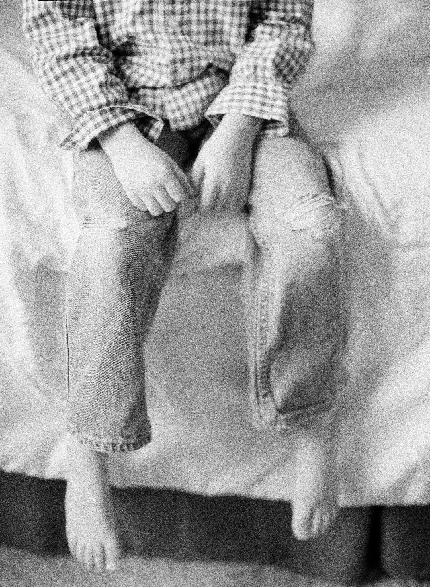 Black and white photo of small feet and legs dangling over white surface.