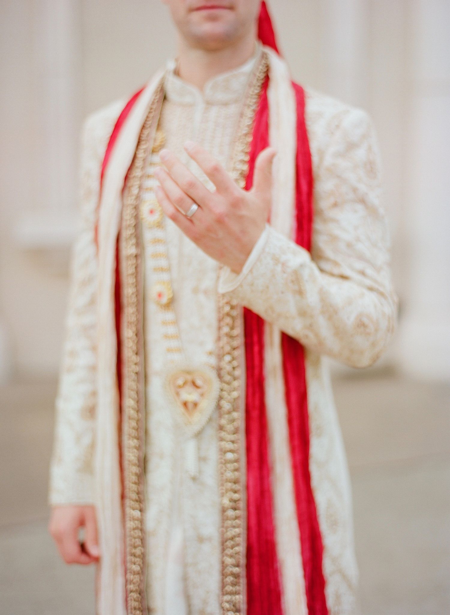 Close-up details of traditional Indian groom's attire featuring cream sherwani with red dupatta.