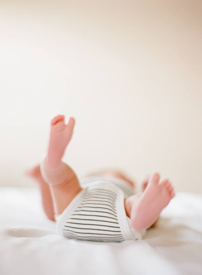 Minimalist photo of baby feet peeking out from striped fabric on white background.