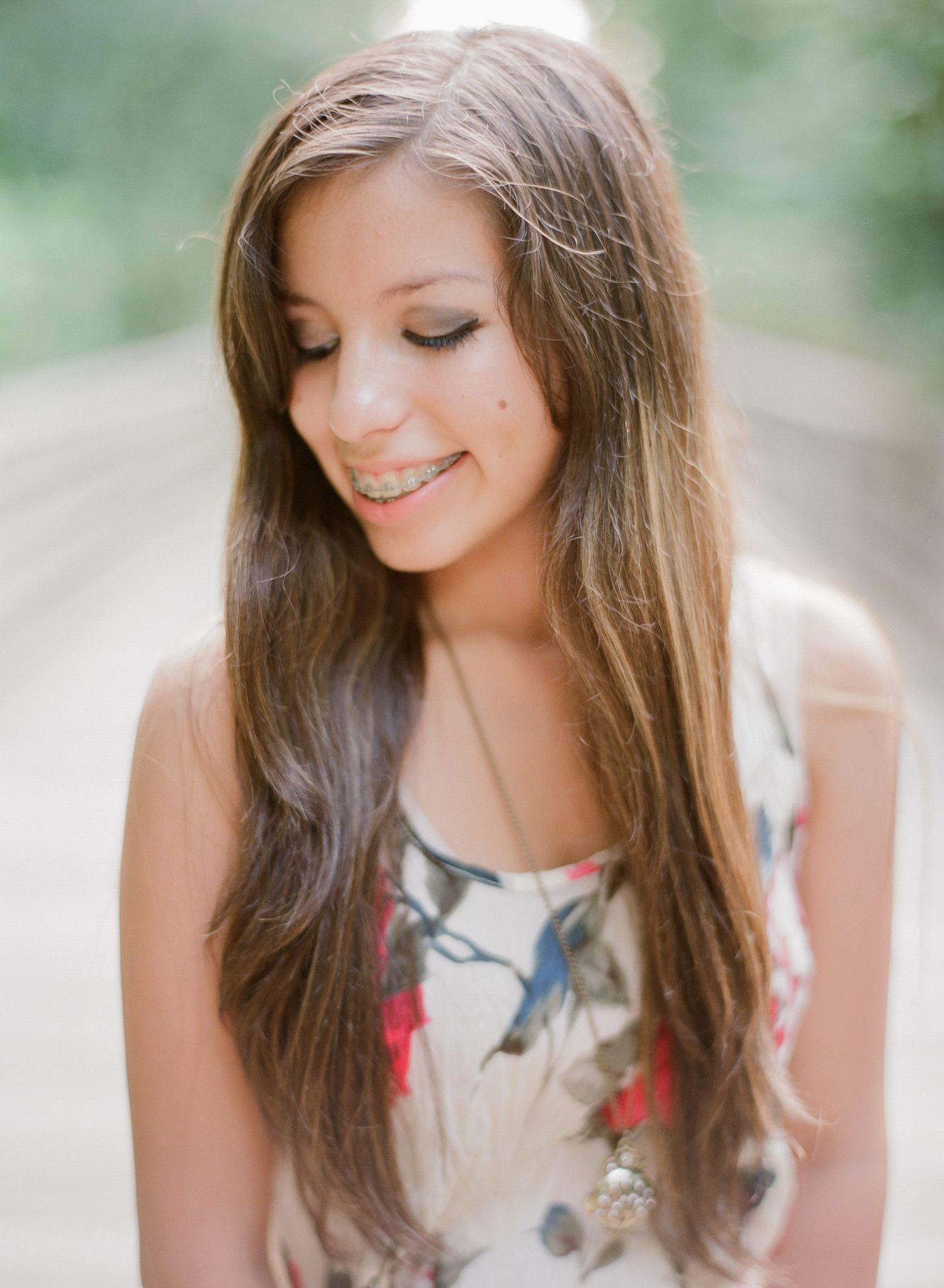 A person wearing a floral dress smiles warmly in an outdoor portrait session.