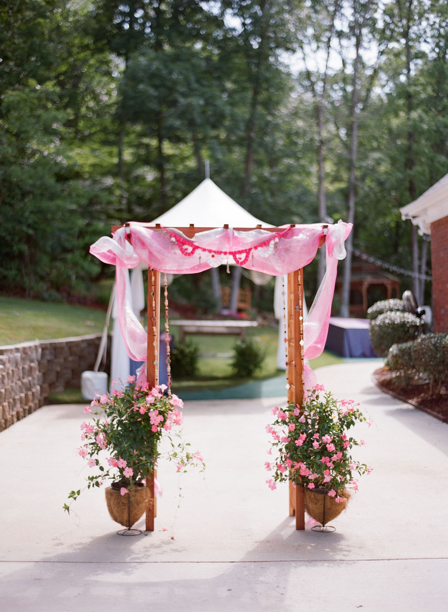 Wedding ceremony aisle decorated with pink fabric draping and floral arrangements on wooden posts.