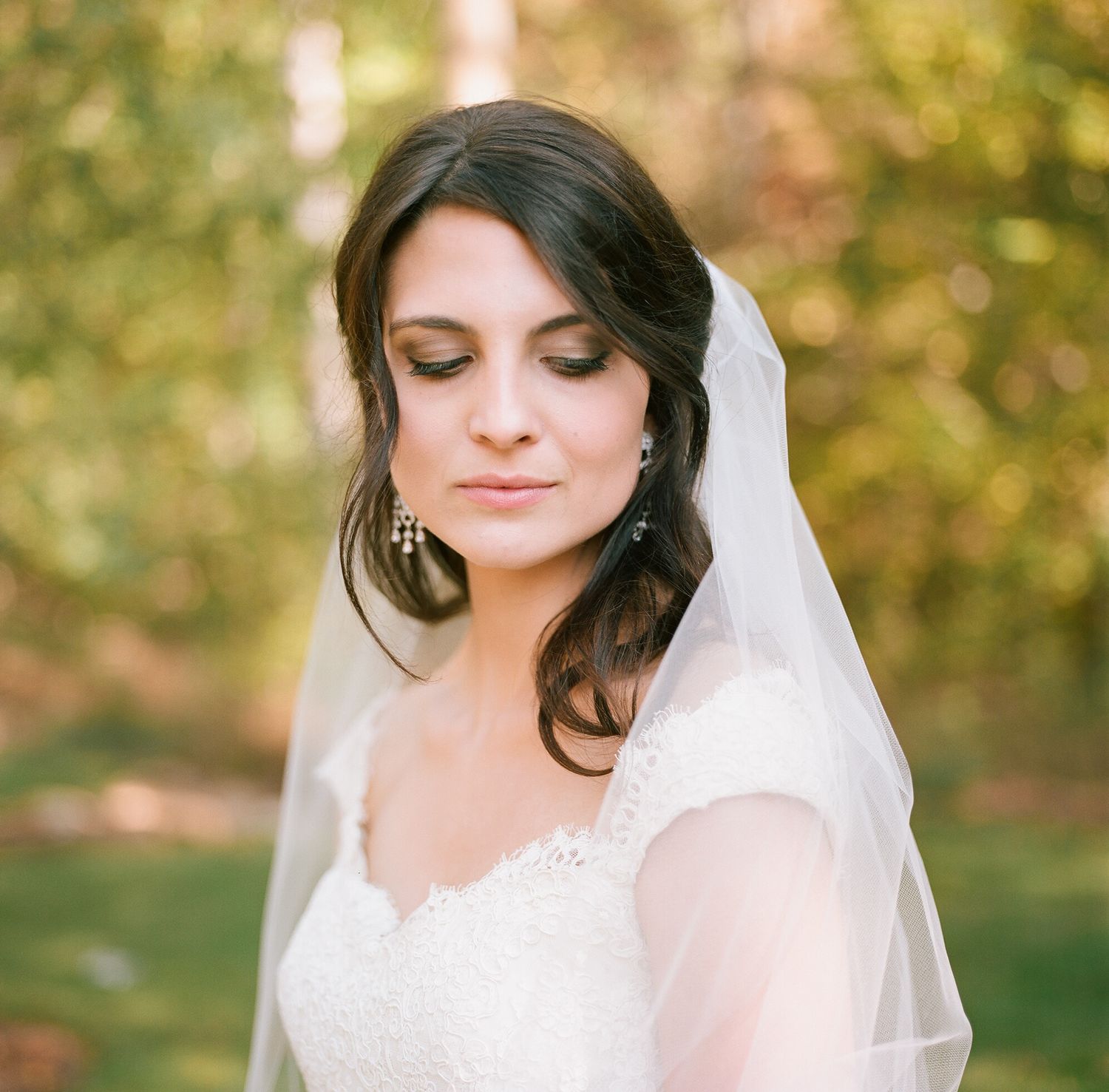Close up portrait of a bride wearing a delicate white veil in a romantic outdoor setting.