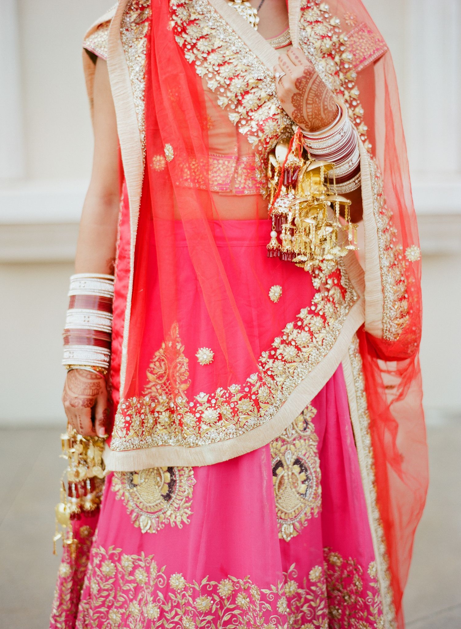 Close-up details of ornate pink and gold embroidered Indian wedding attire with traditional bangles and jewelry.