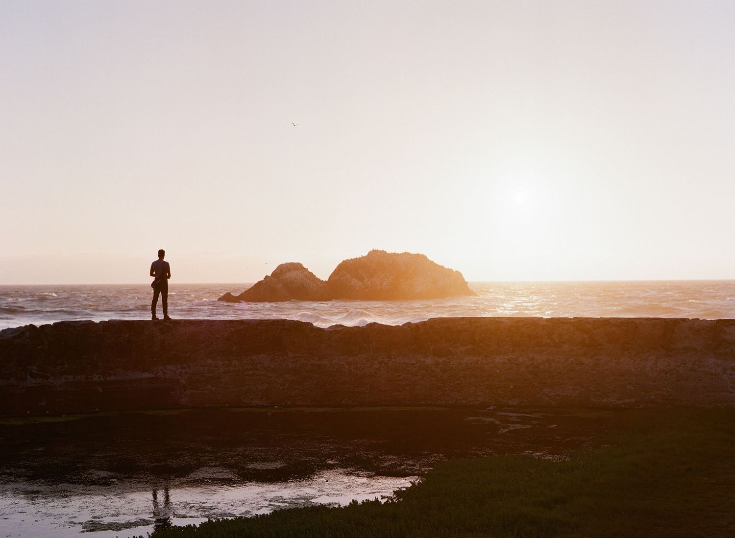 Silhouetted figures against a dramatic ocean sunset with rocky coastline.