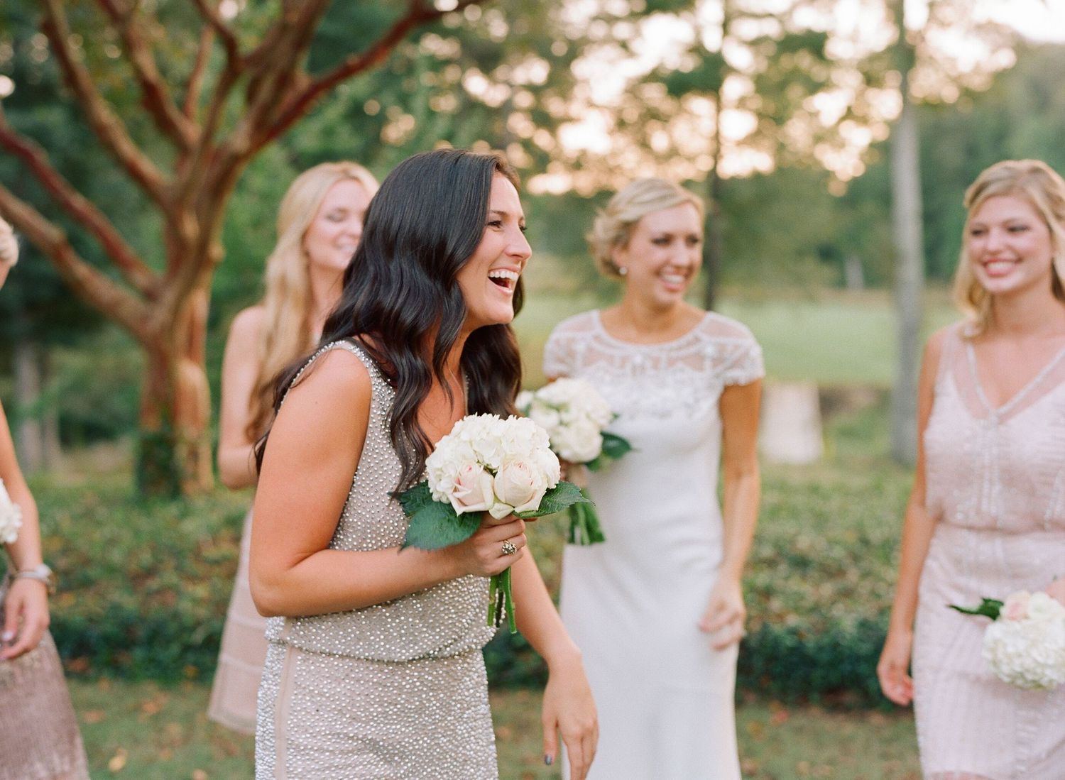 Bridesmaids in sparkly dresses walk together during outdoor wedding celebration.