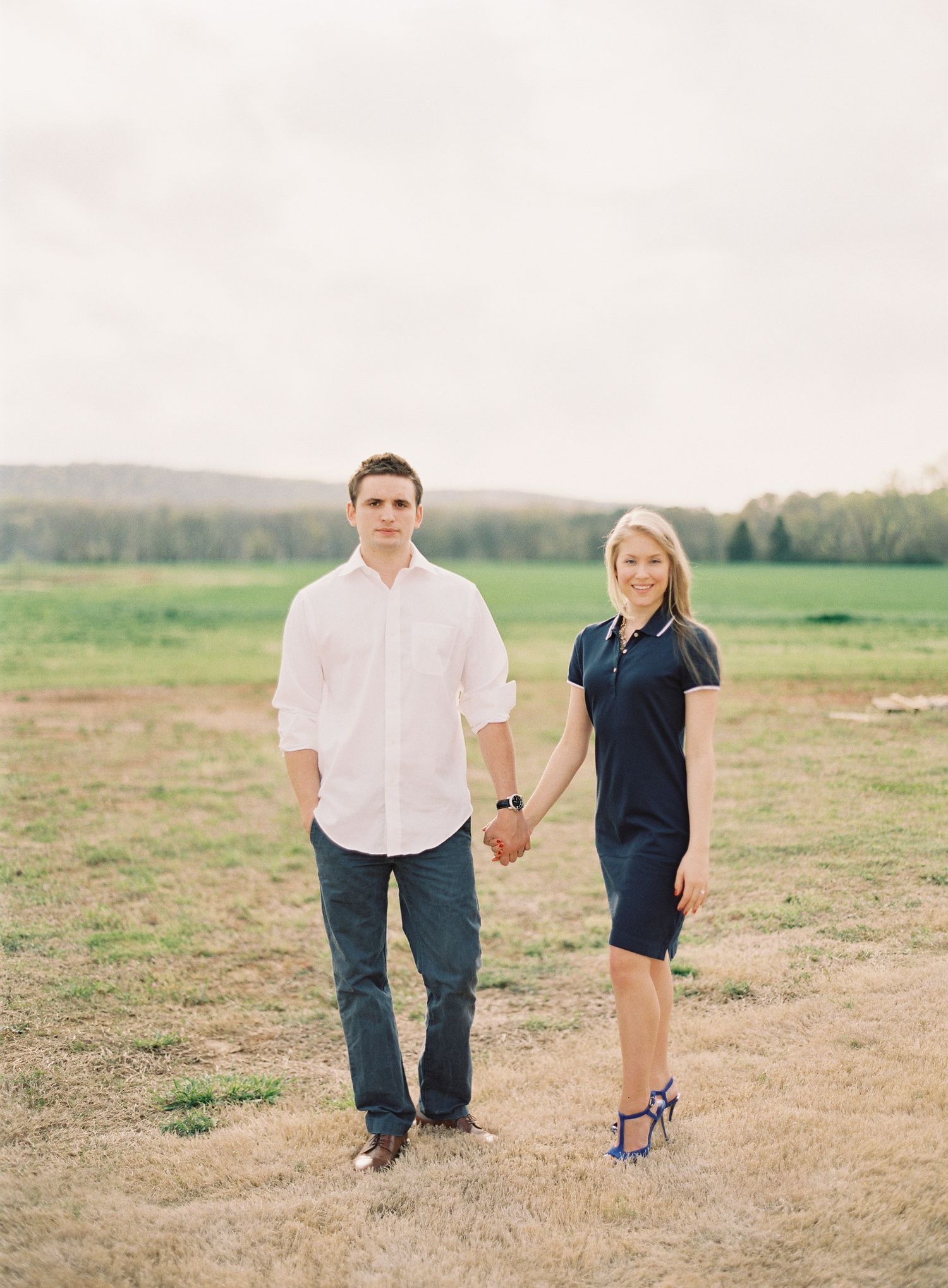 Couple takes a romantic stroll through an open field on a sunny day.