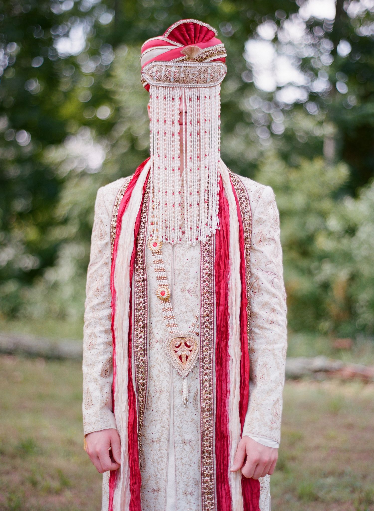 Full-length view of traditional Indian groom's outfit in cream with red accents.
