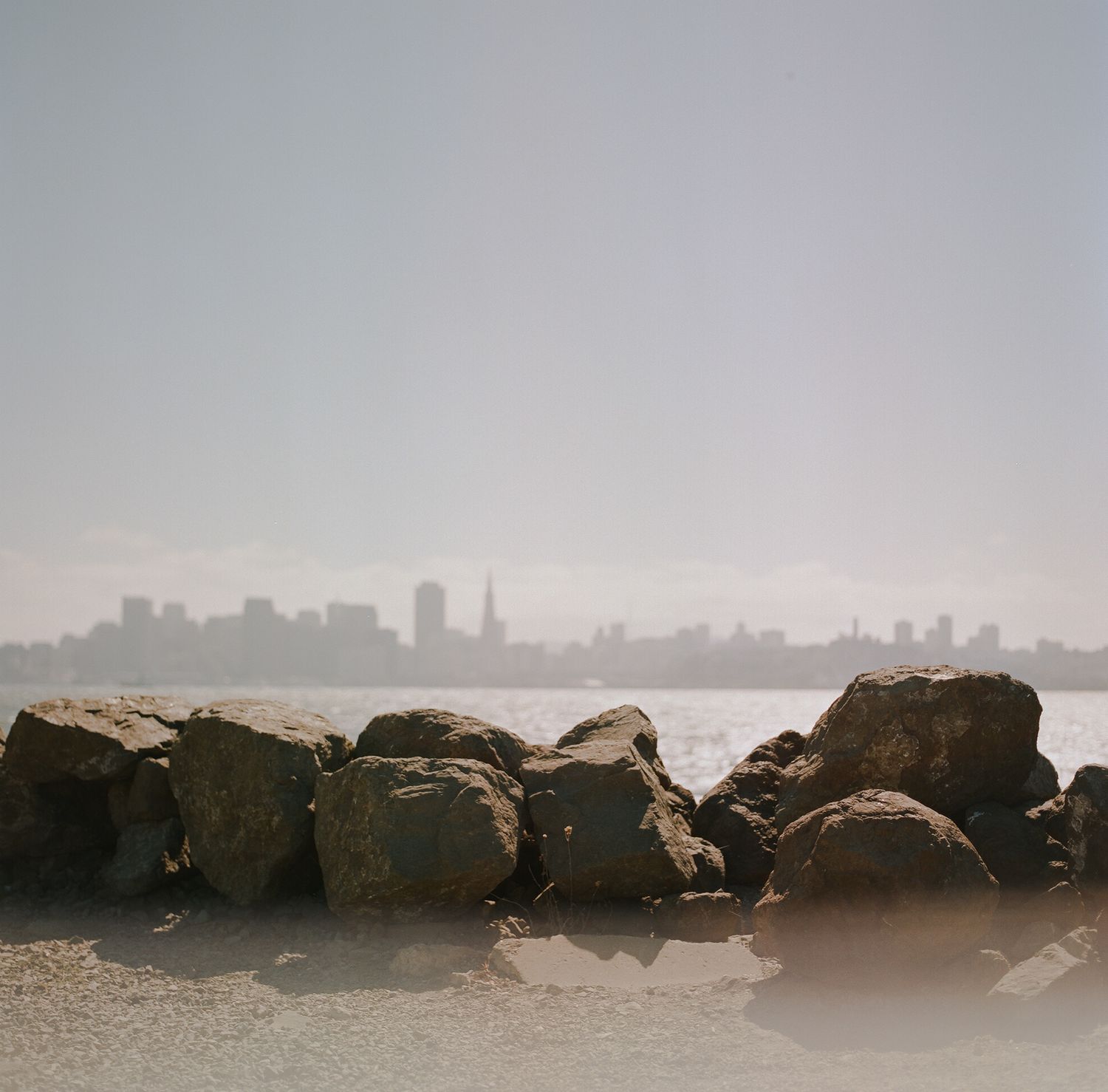 Rocky breakwater with city skyline visible in the misty background.