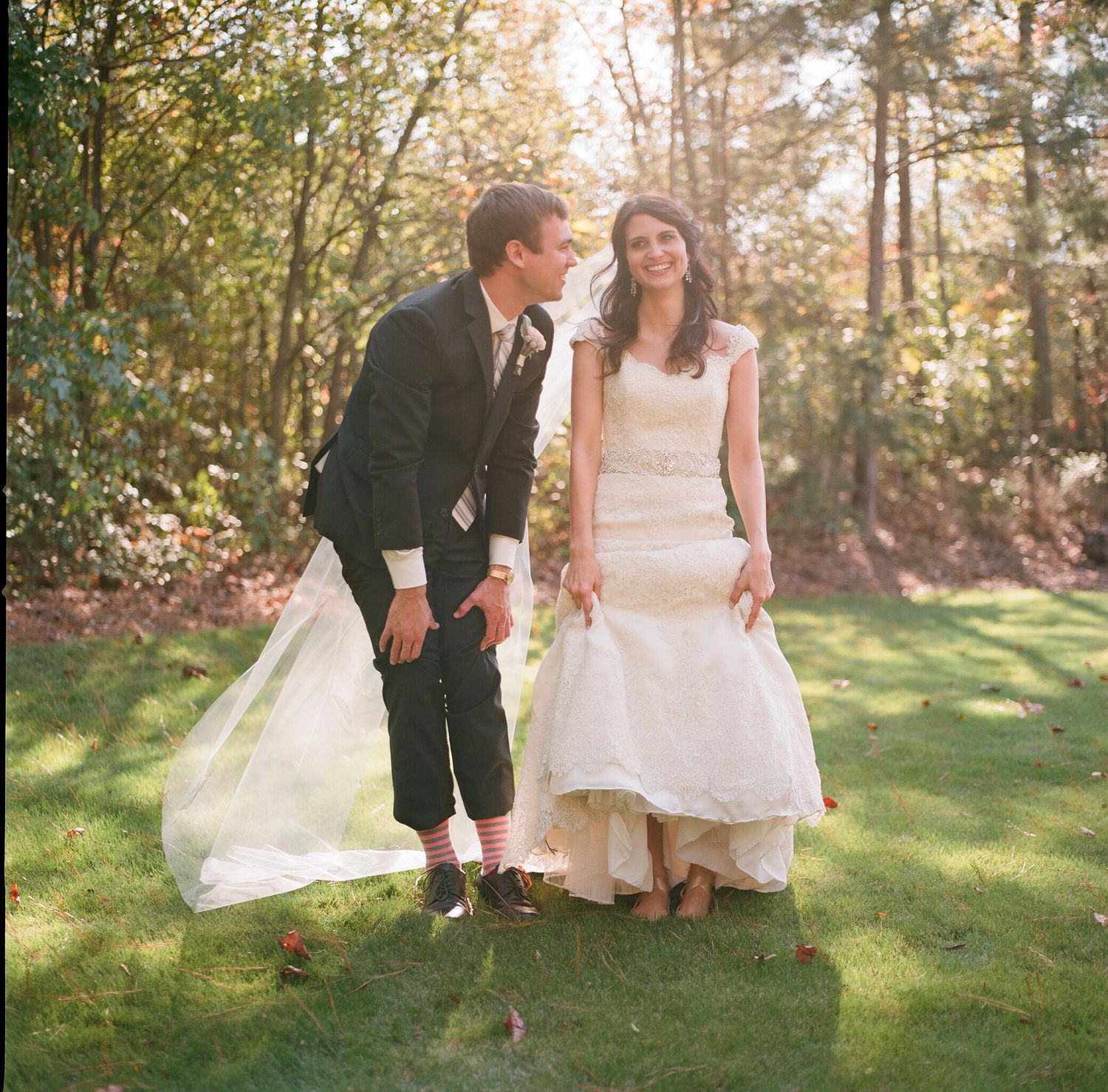 Wedding couple playfully interacting on grass with flowing white dress and veil.