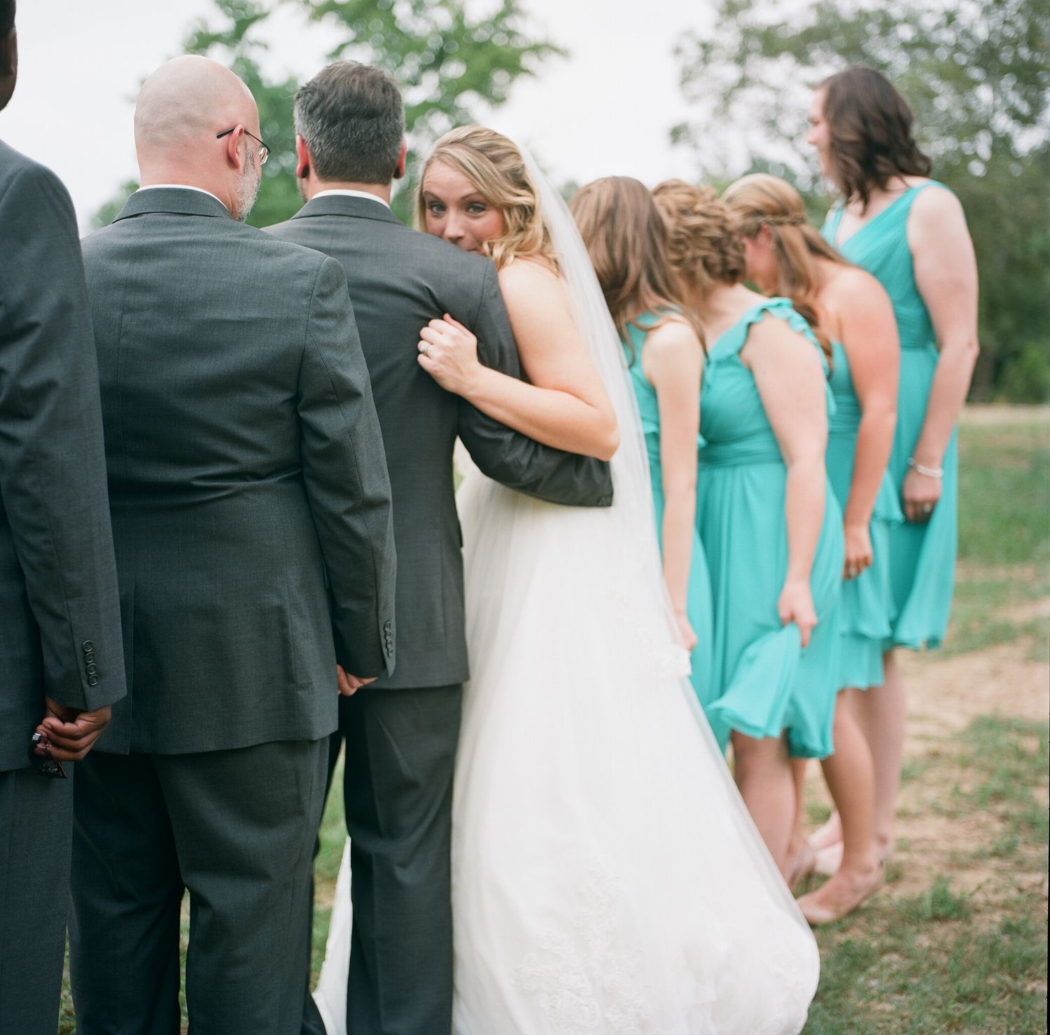 Wedding party in turquoise and gray attire posing together on a garden path.