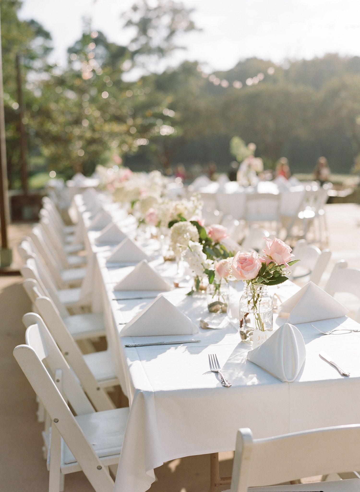 Outdoor wedding reception setup with white folding chairs and elegant table settings.