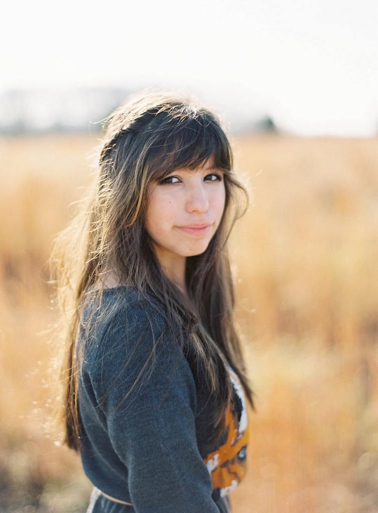 Portrait of woman in dark sweater backlit by golden sunlight in autumn field.