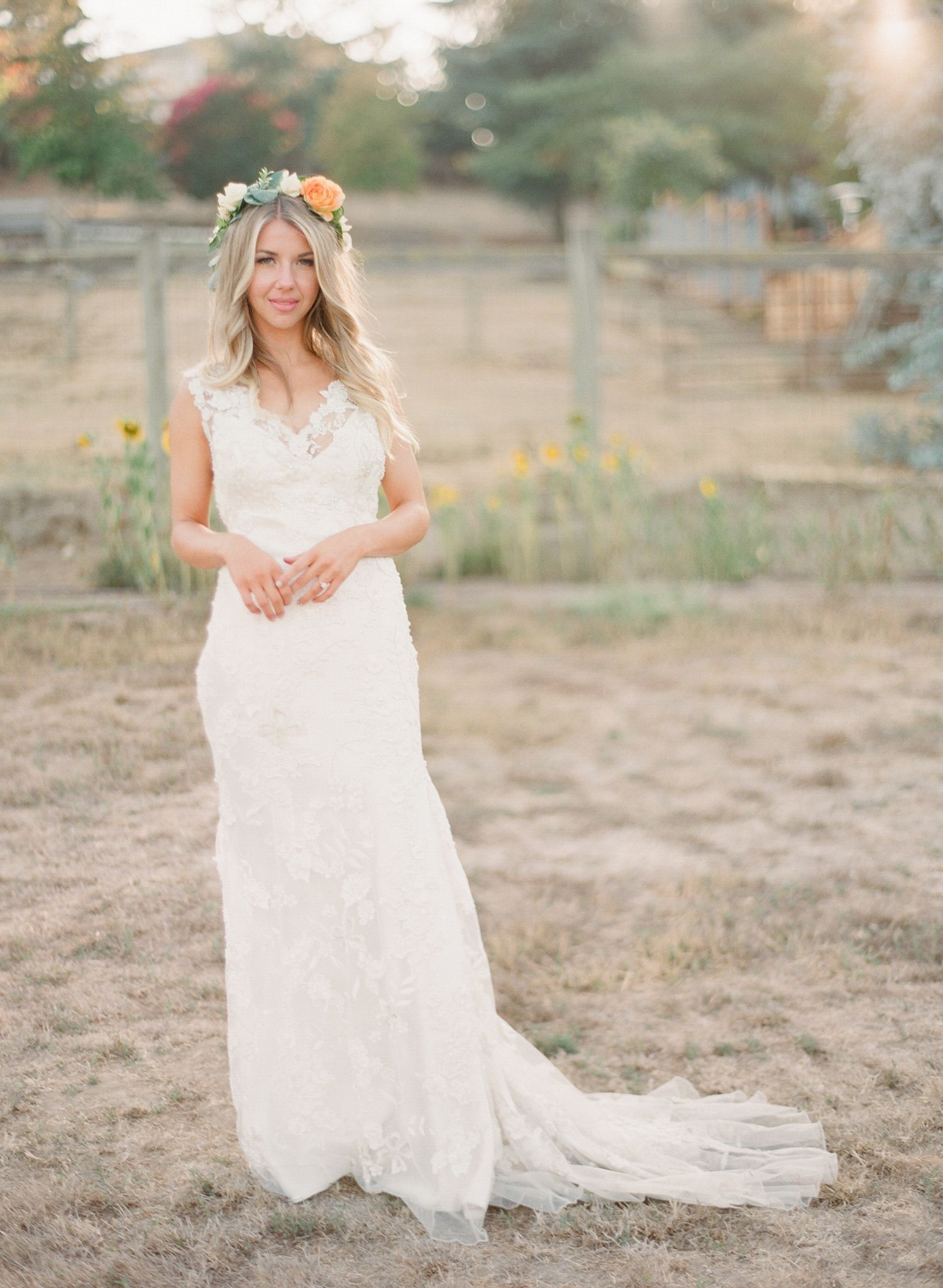 Bride in lace wedding dress posing in an outdoor field setting.