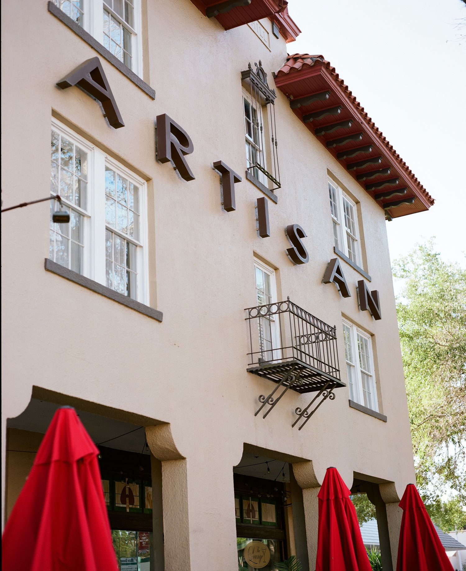 Beige building exterior with red umbrellas and Spanish-style architecture.