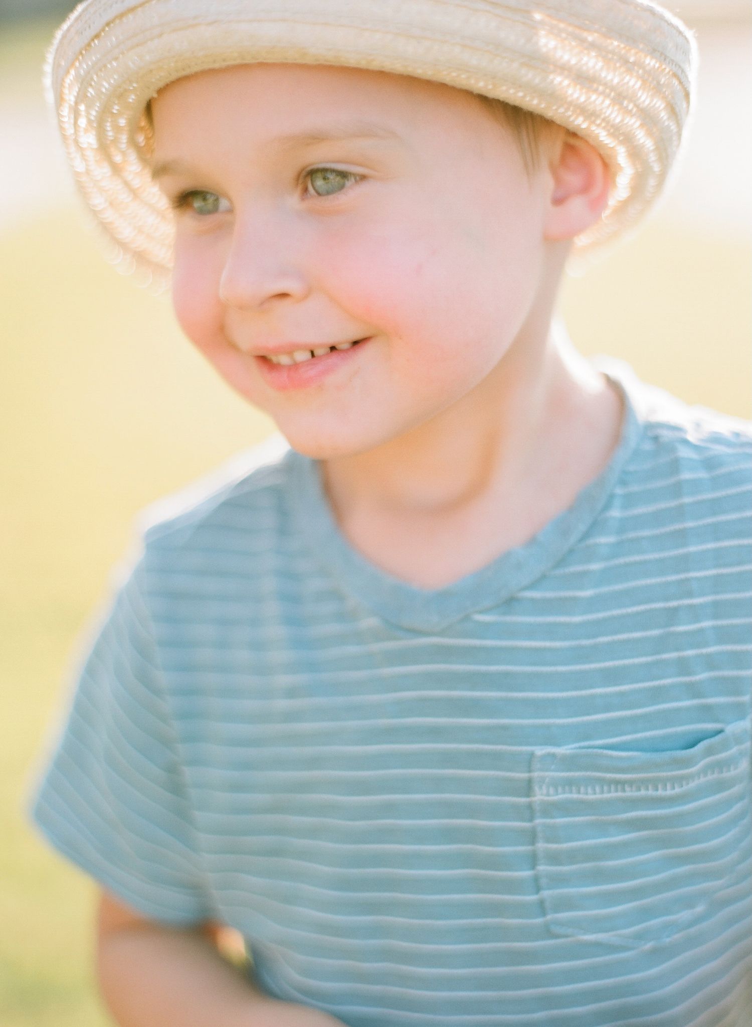Close-up portrait of child wearing striped shirt and light colored hat in warm sunlight.