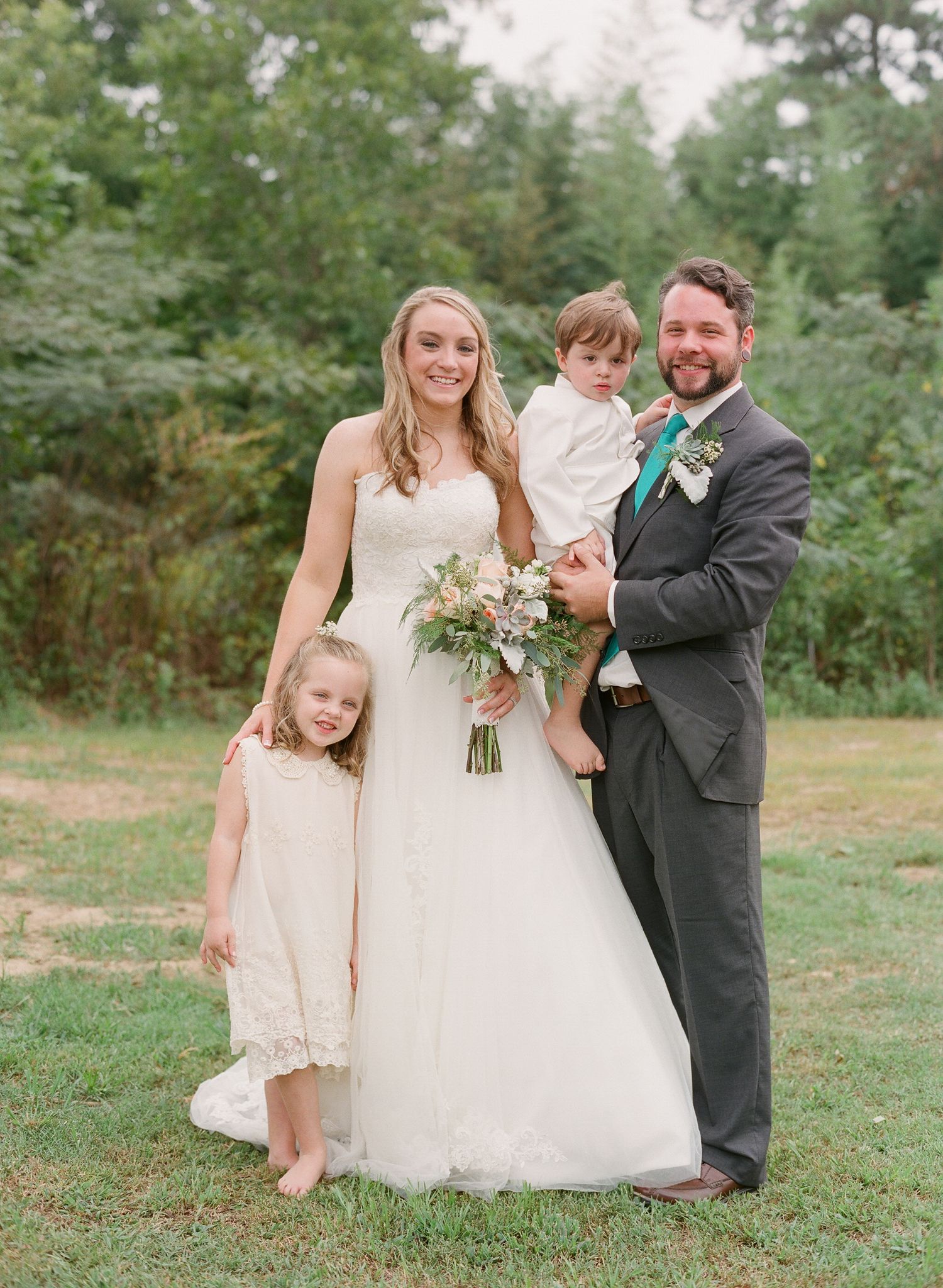Wedding party shares candid moment on grassy field during outdoor celebration.