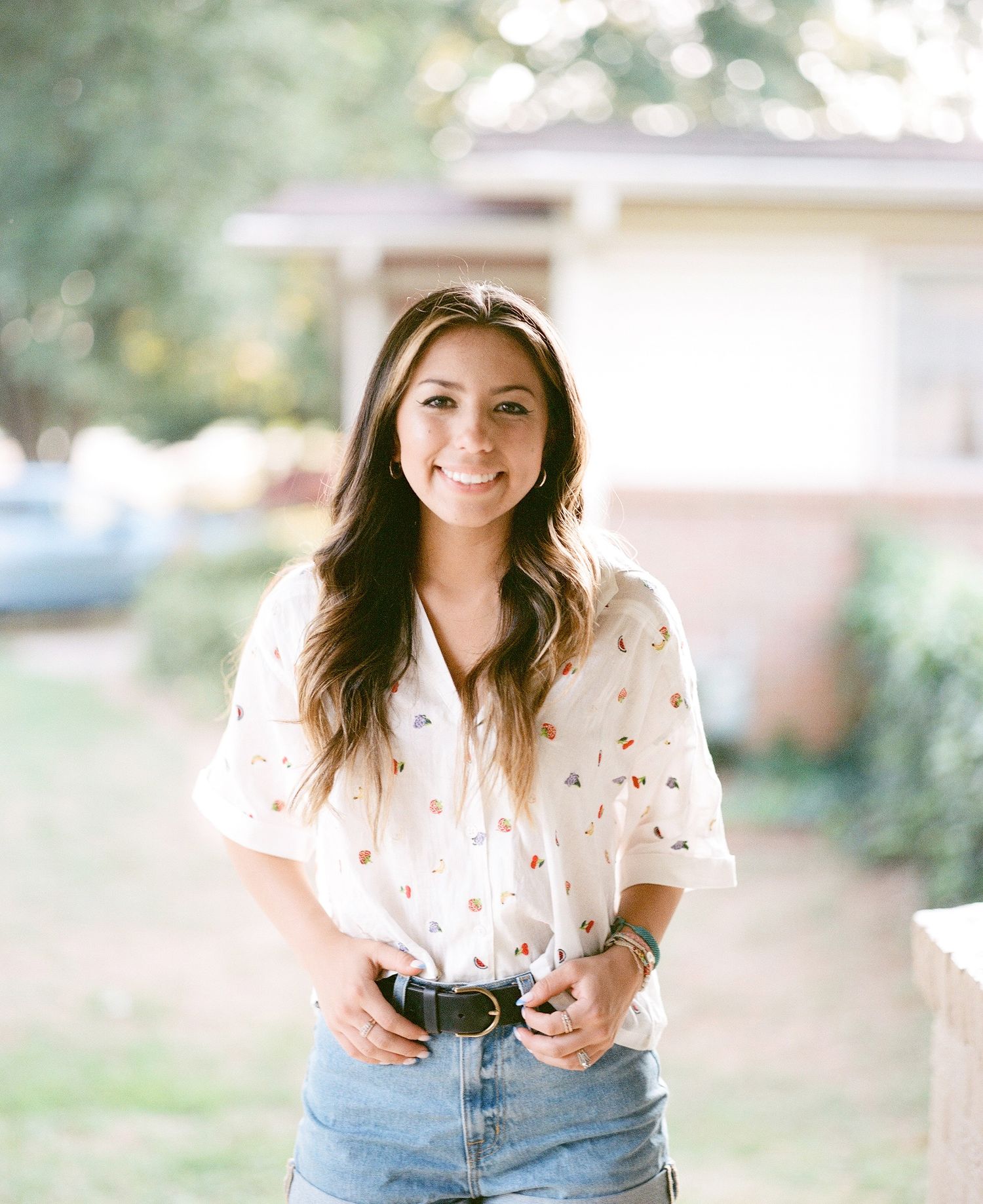 A person in casual clothing sits outdoors smiling in natural lighting.