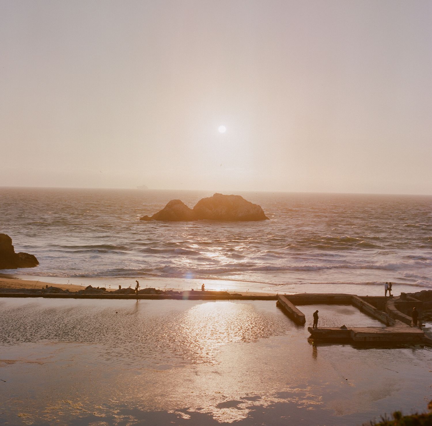 Panoramic coastal sunset view with waves crashing against rocky outcrops.