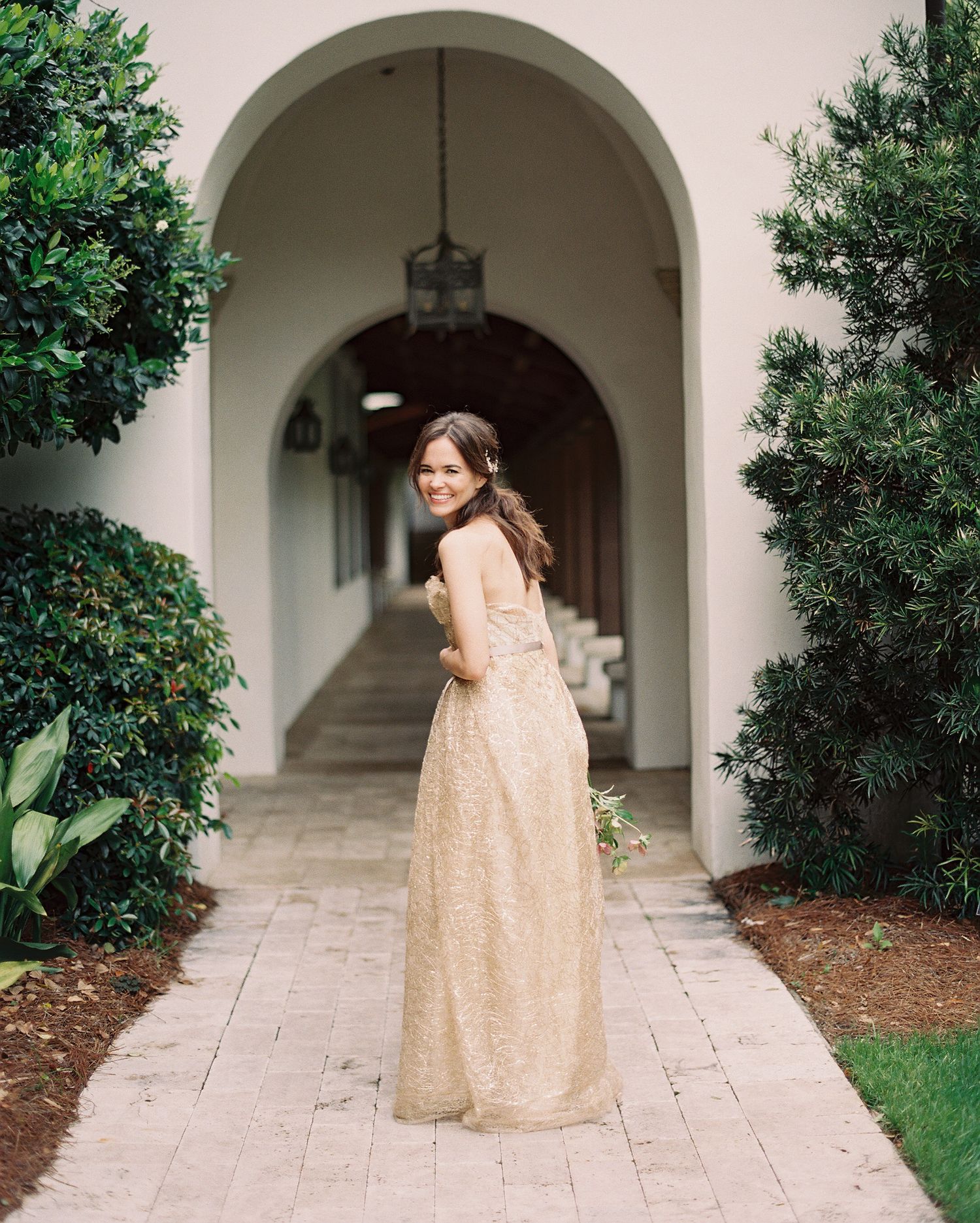 Person in champagne-colored gown walks through arched colonnade.