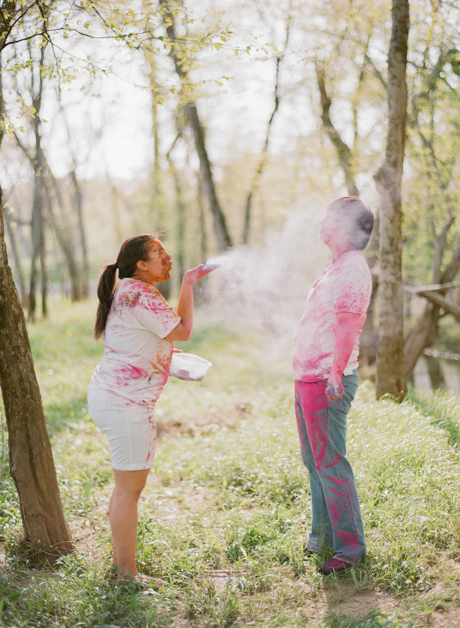 People playing with colorful pink powder in a wooded area during what appears to be a color run or Holi celebration.