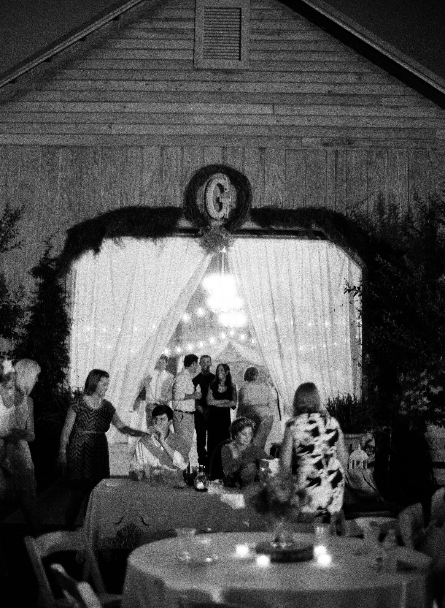 Wedding reception scene inside a rustic barn venue with white draping and ambient lighting.