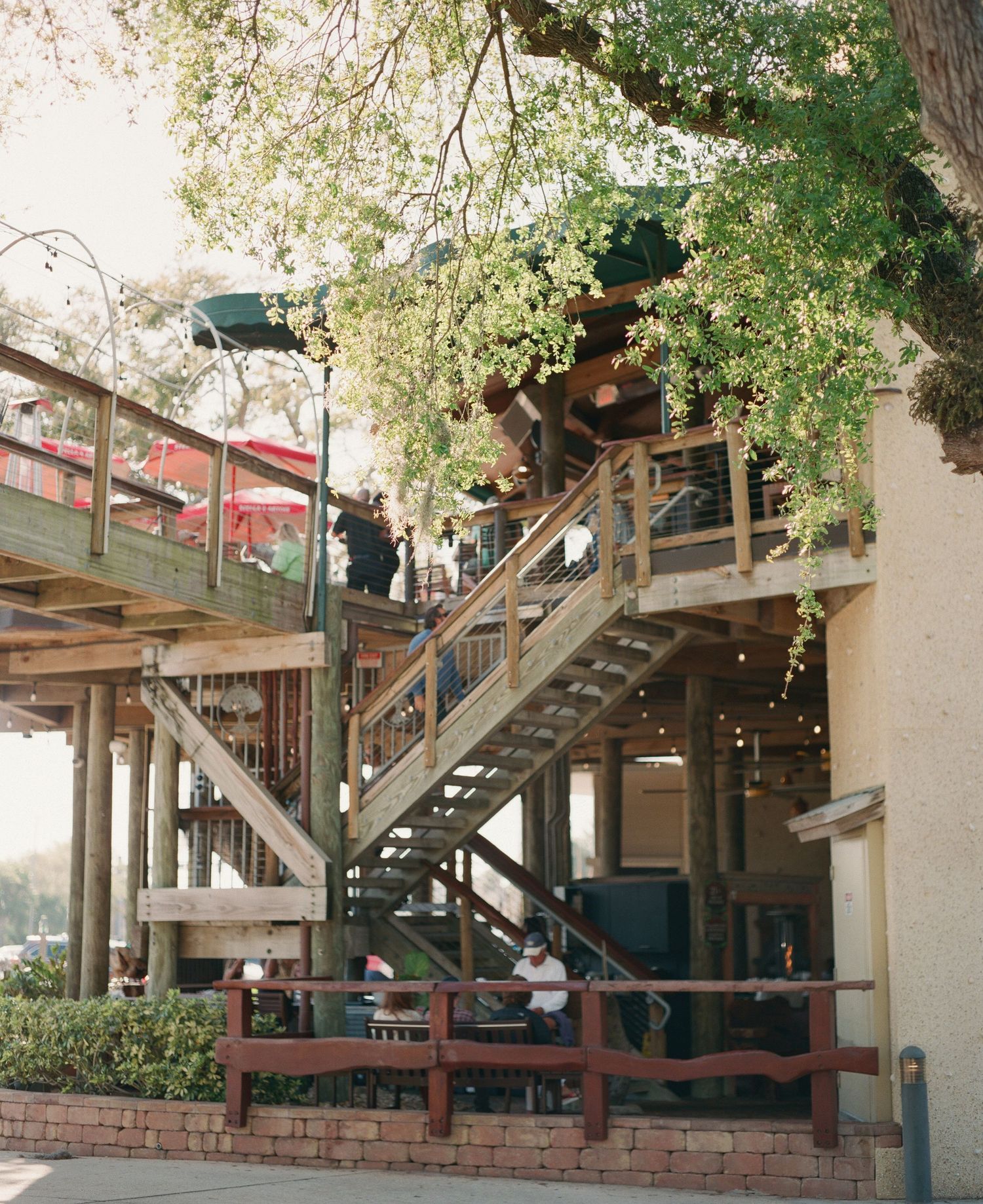 Multi-level wooden deck restaurant with outdoor staircases surrounded by large trees in a rustic setting.