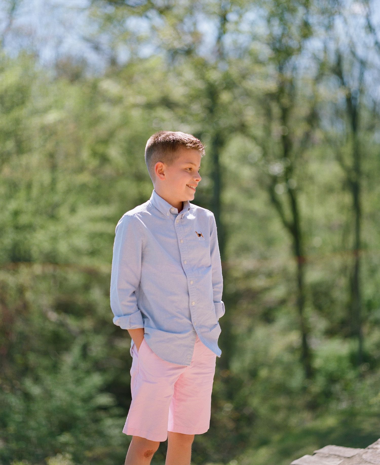 Young boy in light colored clothing walking through a sunny outdoor setting.