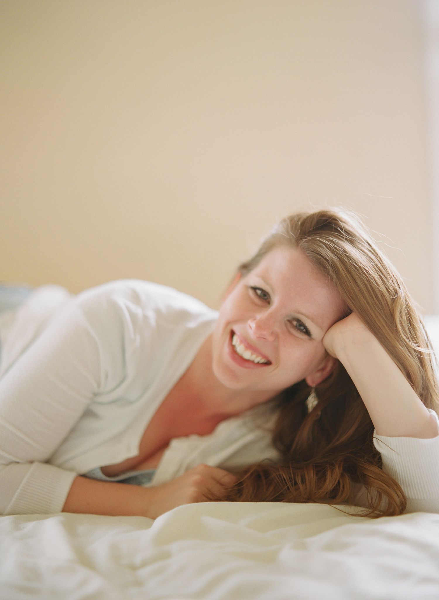Intimate lifestyle portrait of someone relaxing on white bedding in natural light.