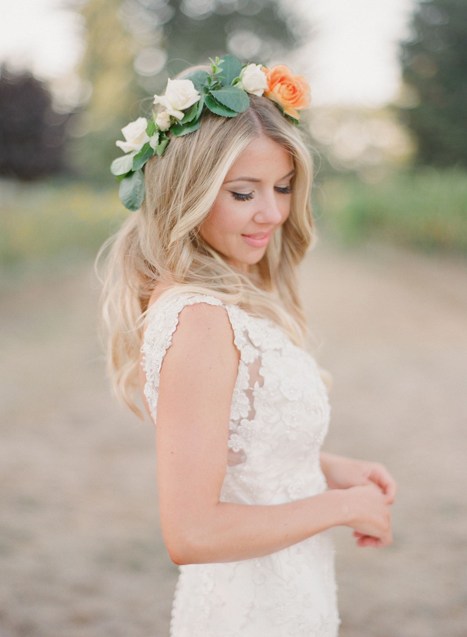 Bride wearing a floral crown and lace dress poses in soft natural light.