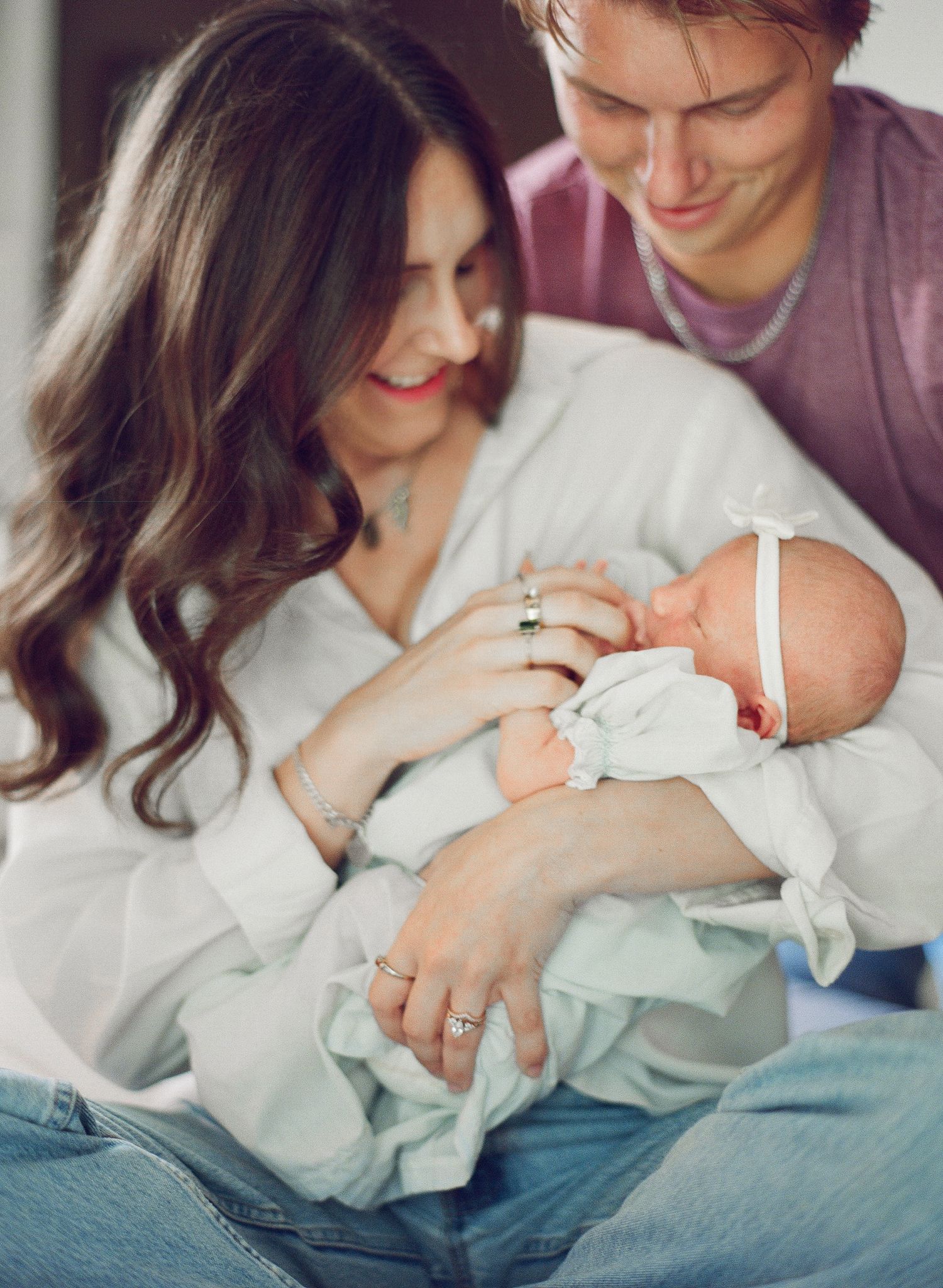 Young couple smiling and cradling their newborn baby wrapped in white, sharing a tender family moment.