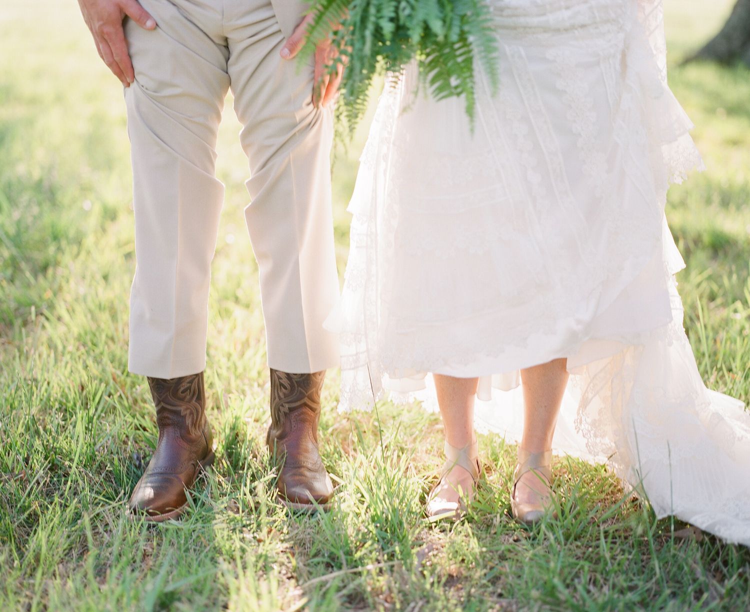 Row of bare feet standing in grass beside flowing white wedding dress.